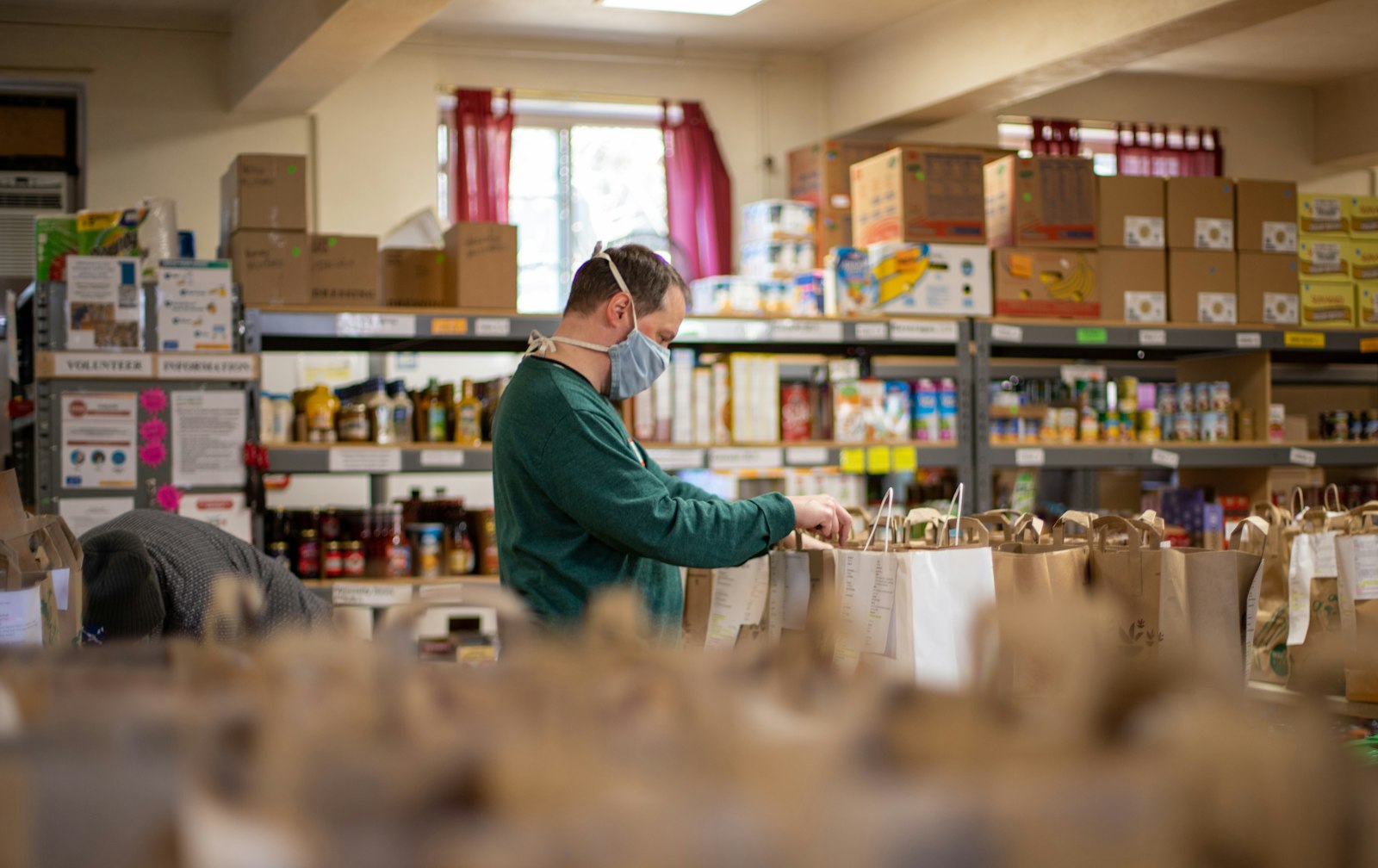 A volunteer filling bags in a food bank storeroom with stocked shelves