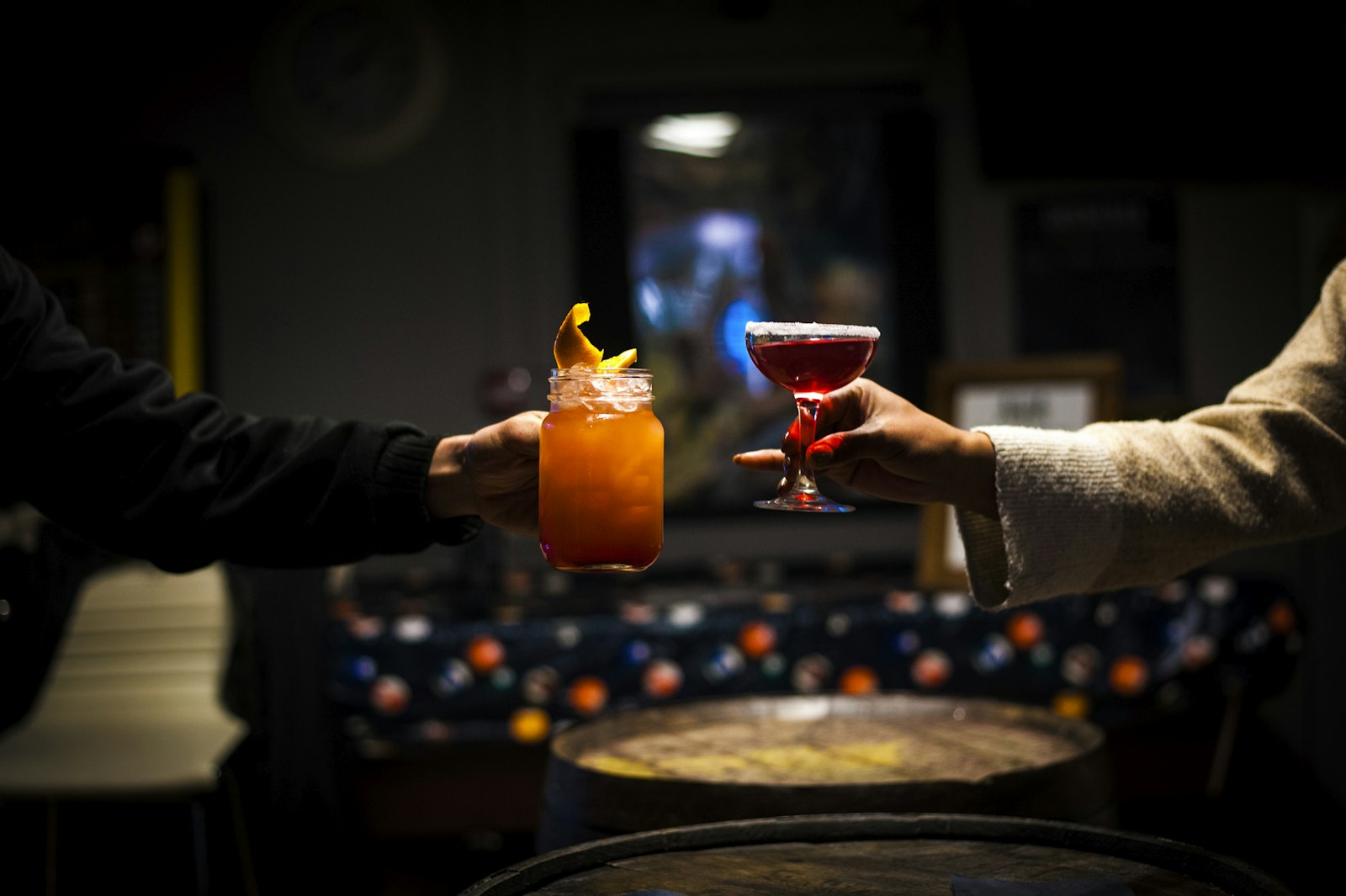 Two cocktails clinking in a dark bar