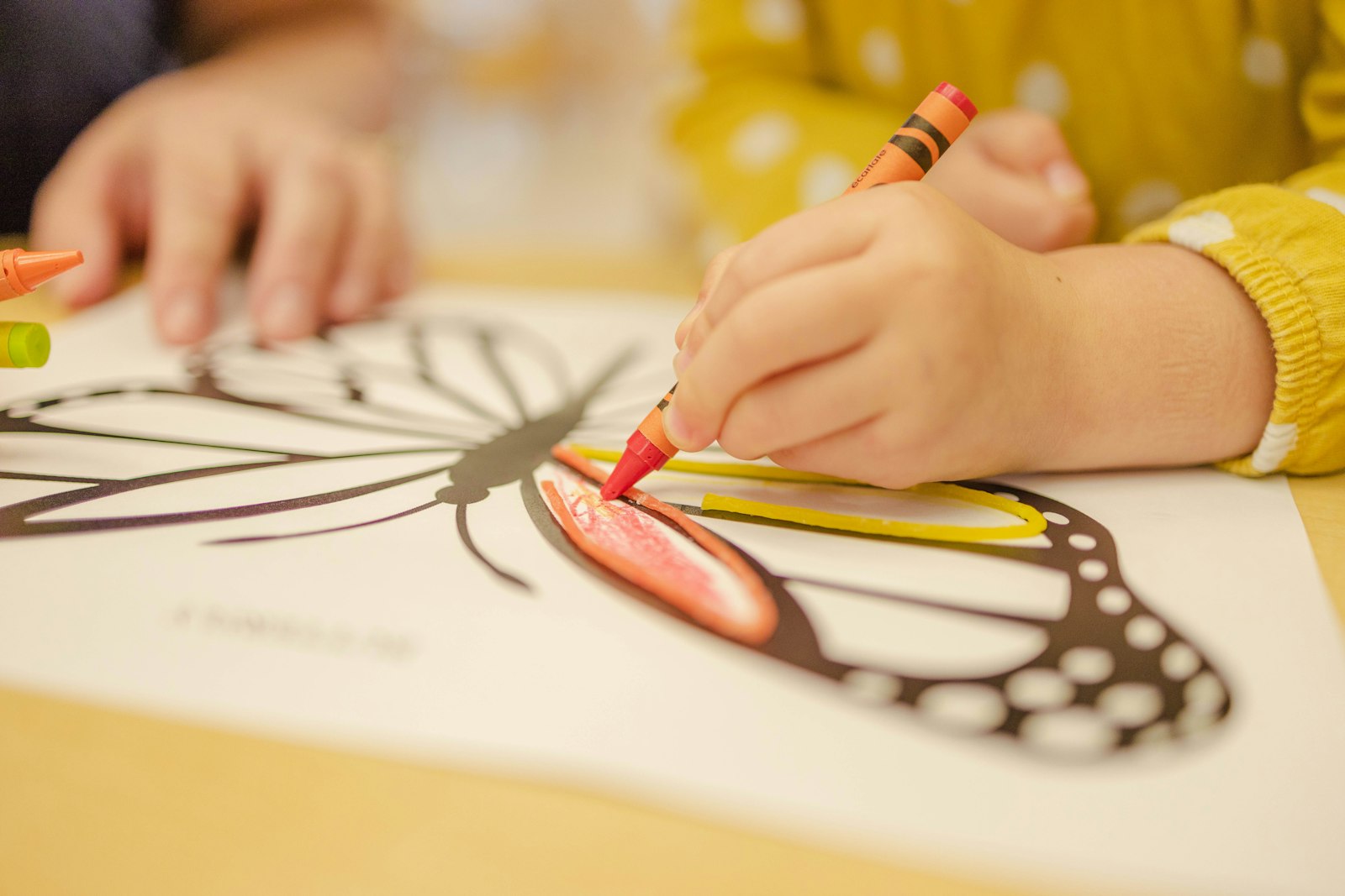 A small hand colouring a butterfly with a red crayon