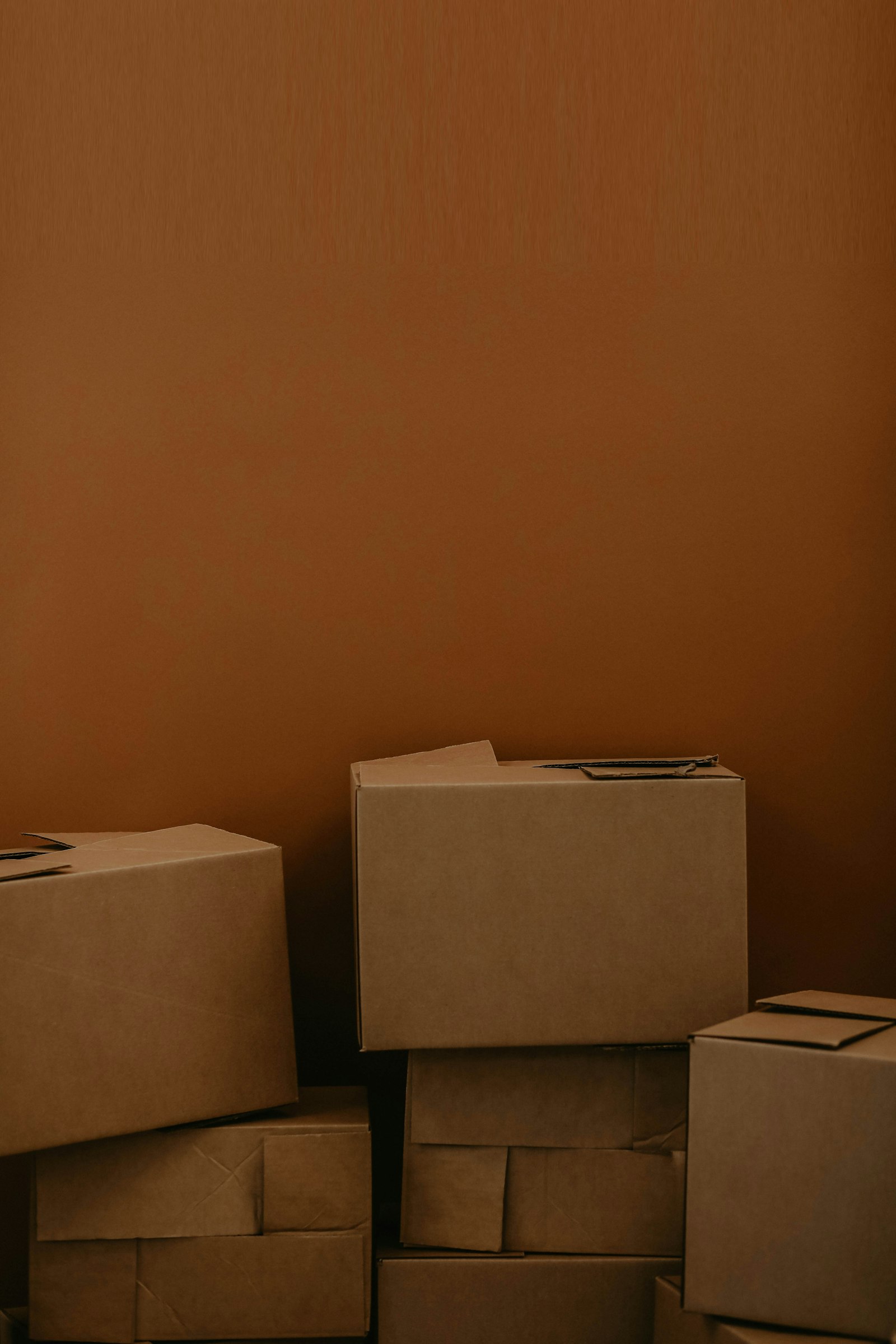 A stack of plain cardboard boxes against a warm brown wall