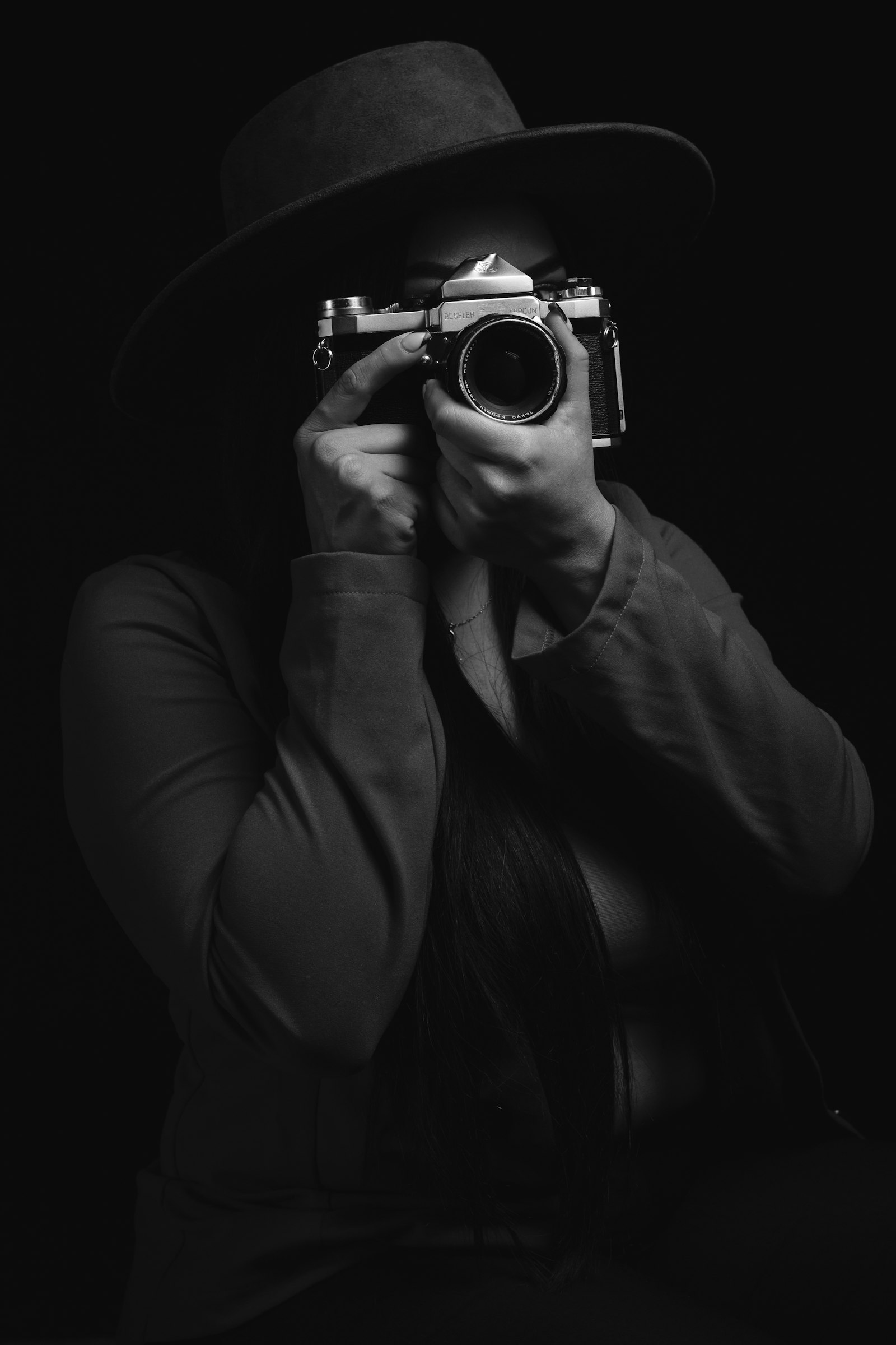 A woman in a hat holding a camera to her eye, black and white