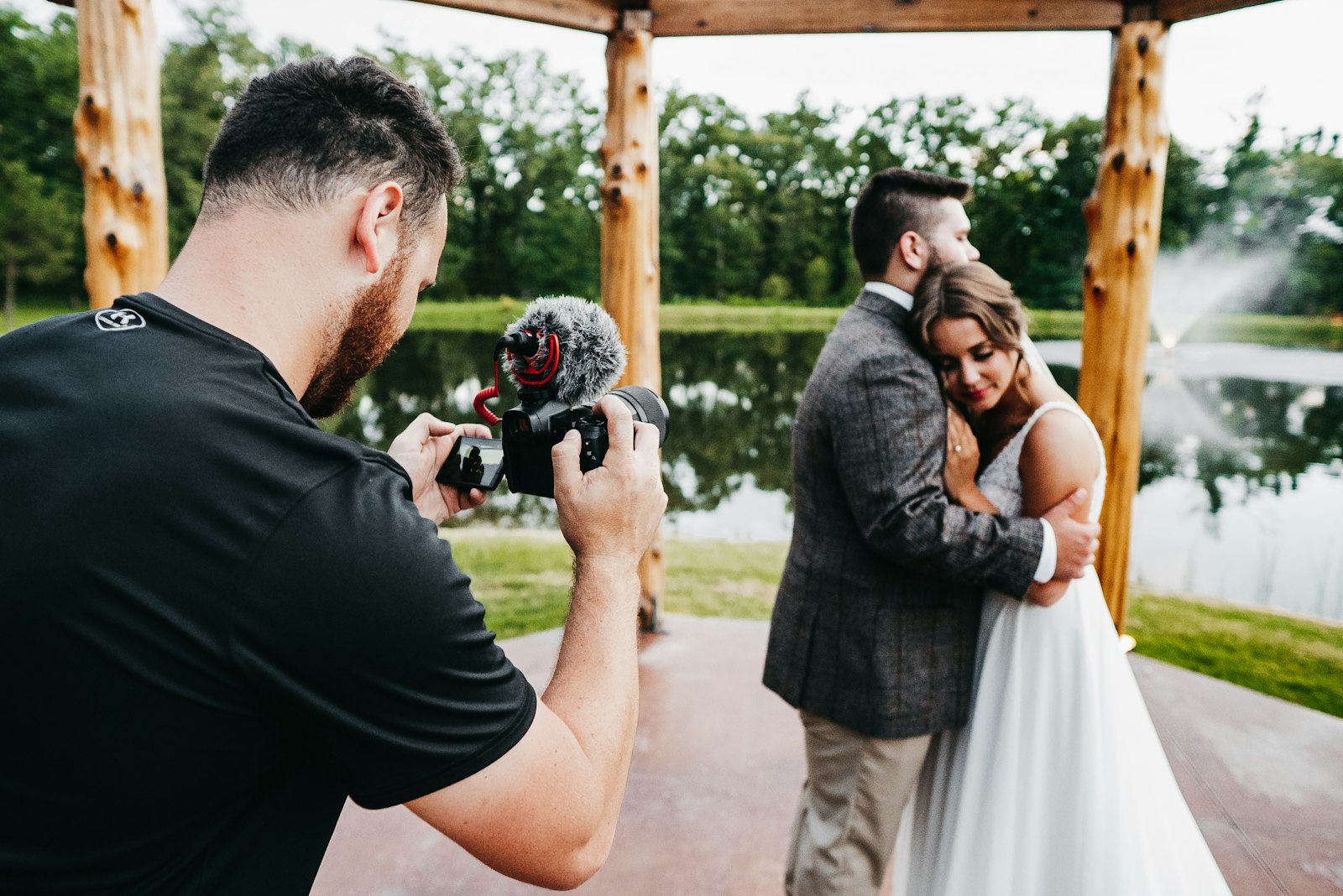 A wedding couple under a wooden arch, the photographer in frame