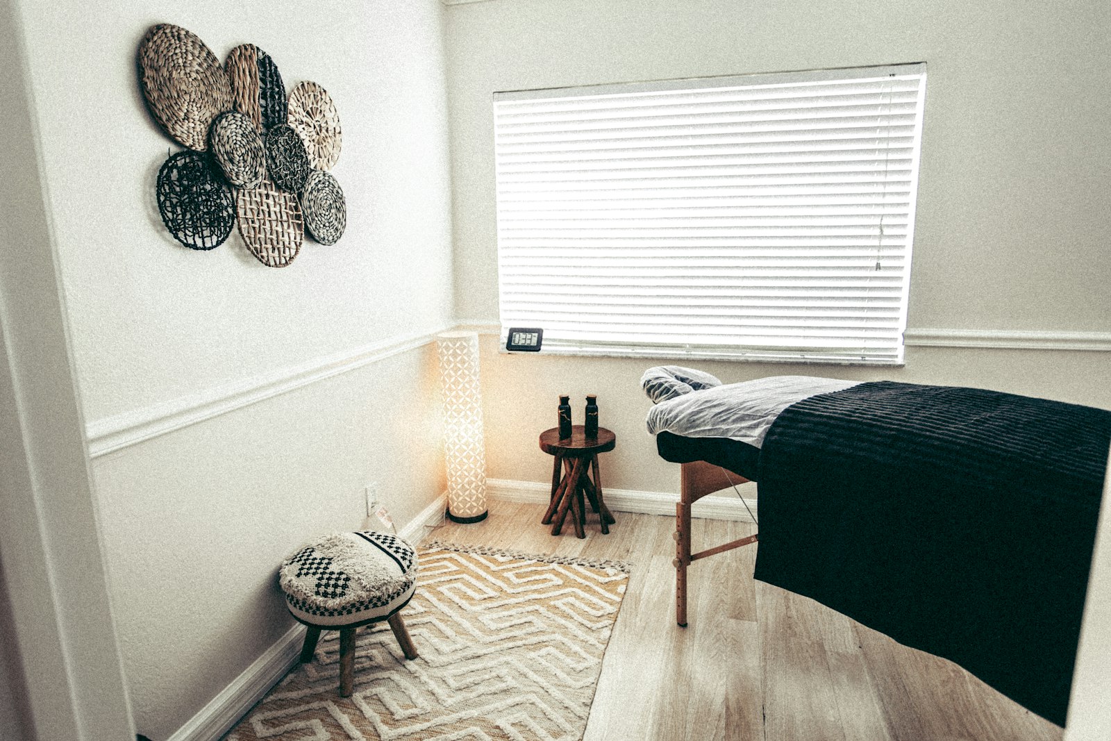A small treatment room with a massage table under a blind-covered window