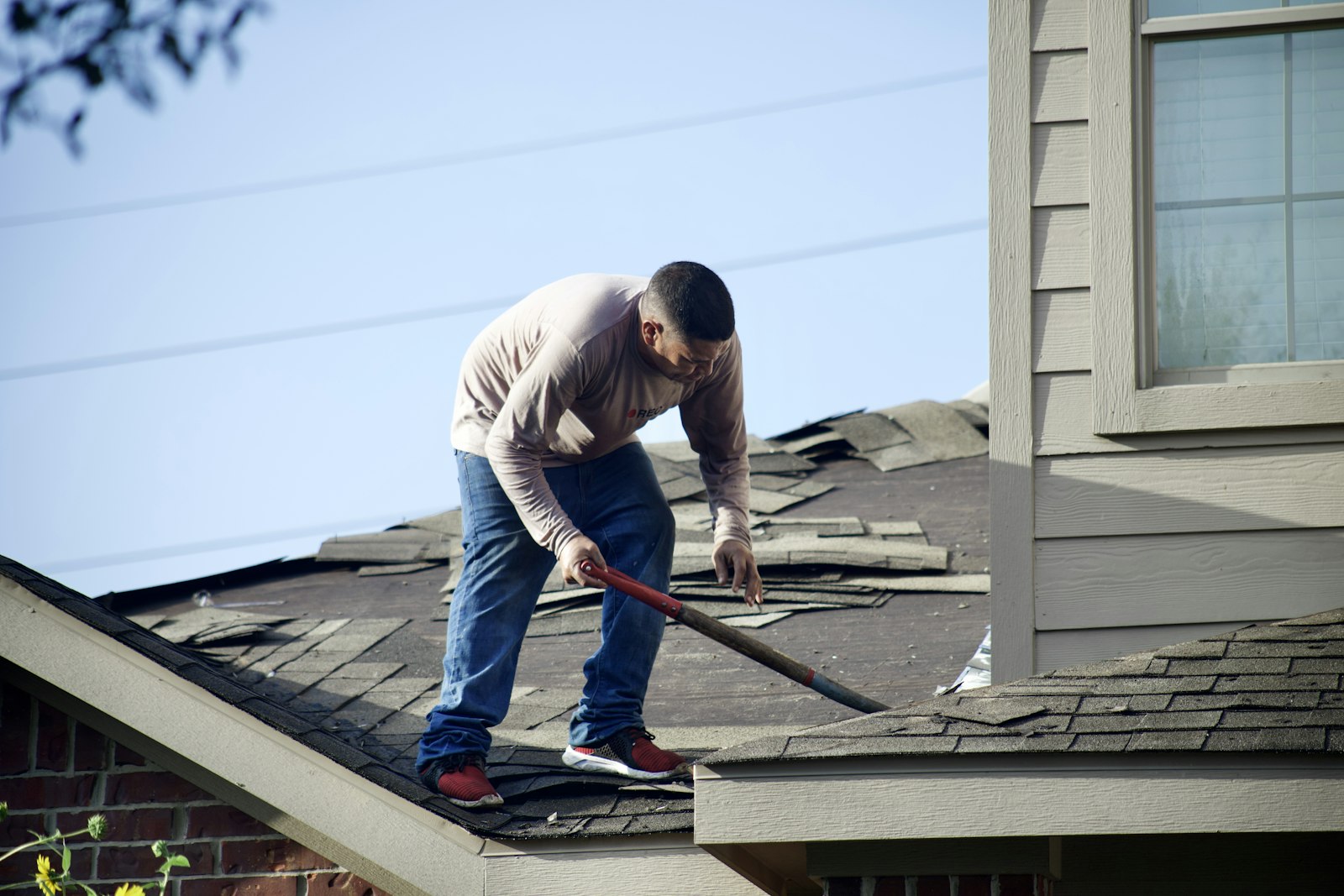 A roofer stripping old shingles from a pitched roof