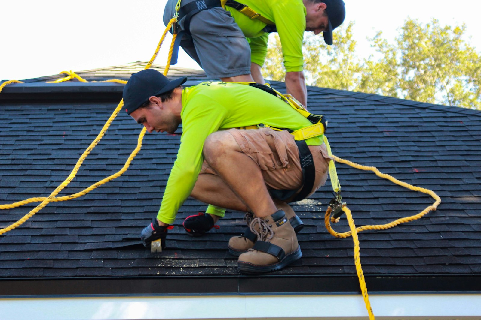 Two roofers in hi-vis shirts and safety ropes fixing shingles