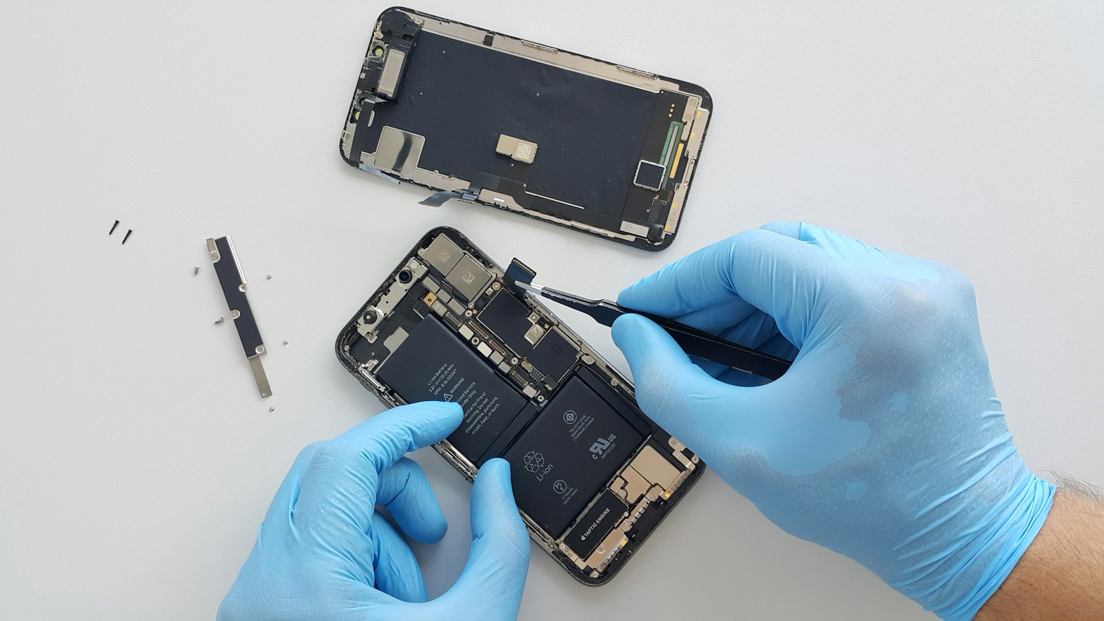 Gloved hands with tweezers on an open phone beside its screen