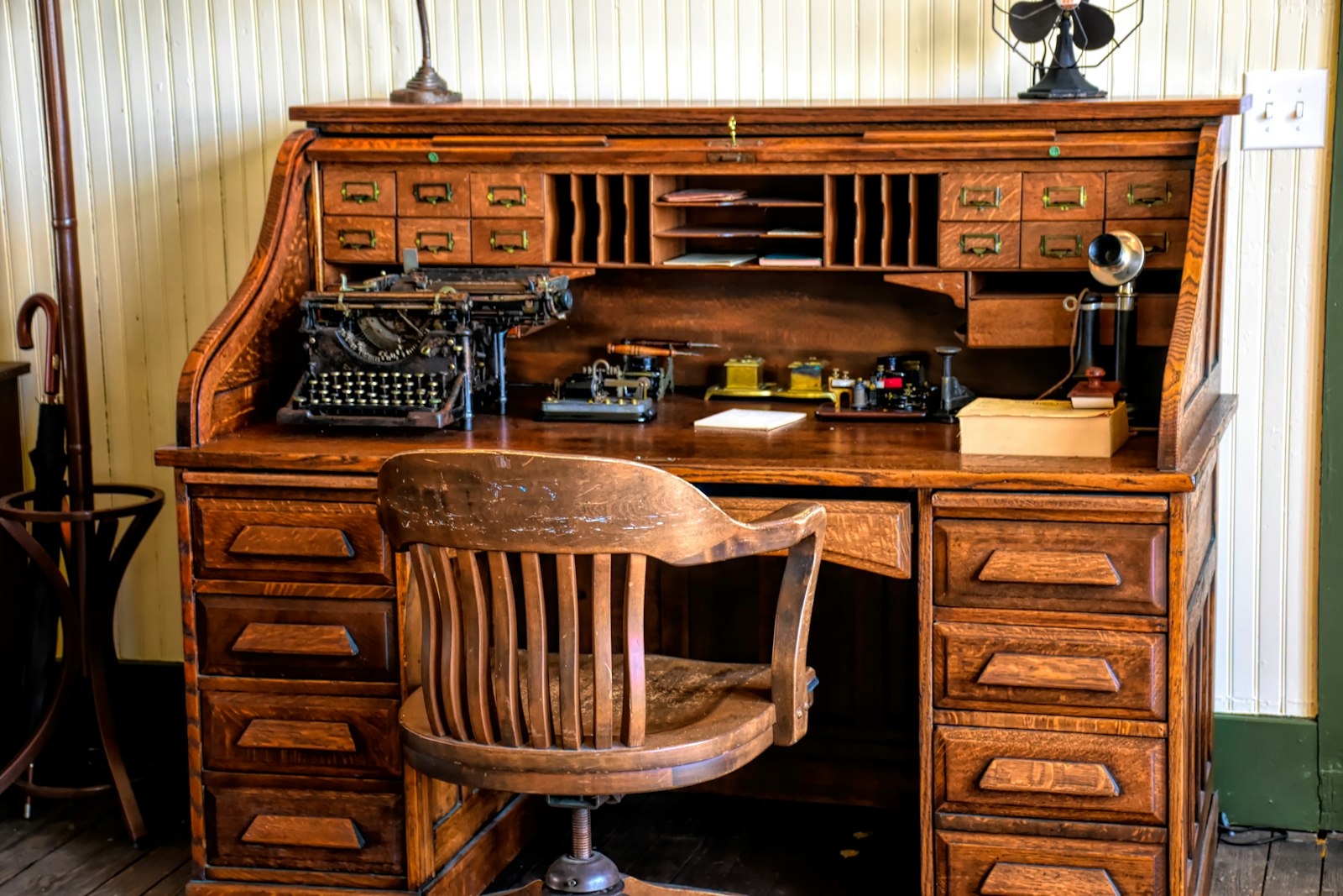 A roll-top desk with a typewriter and a wooden chair