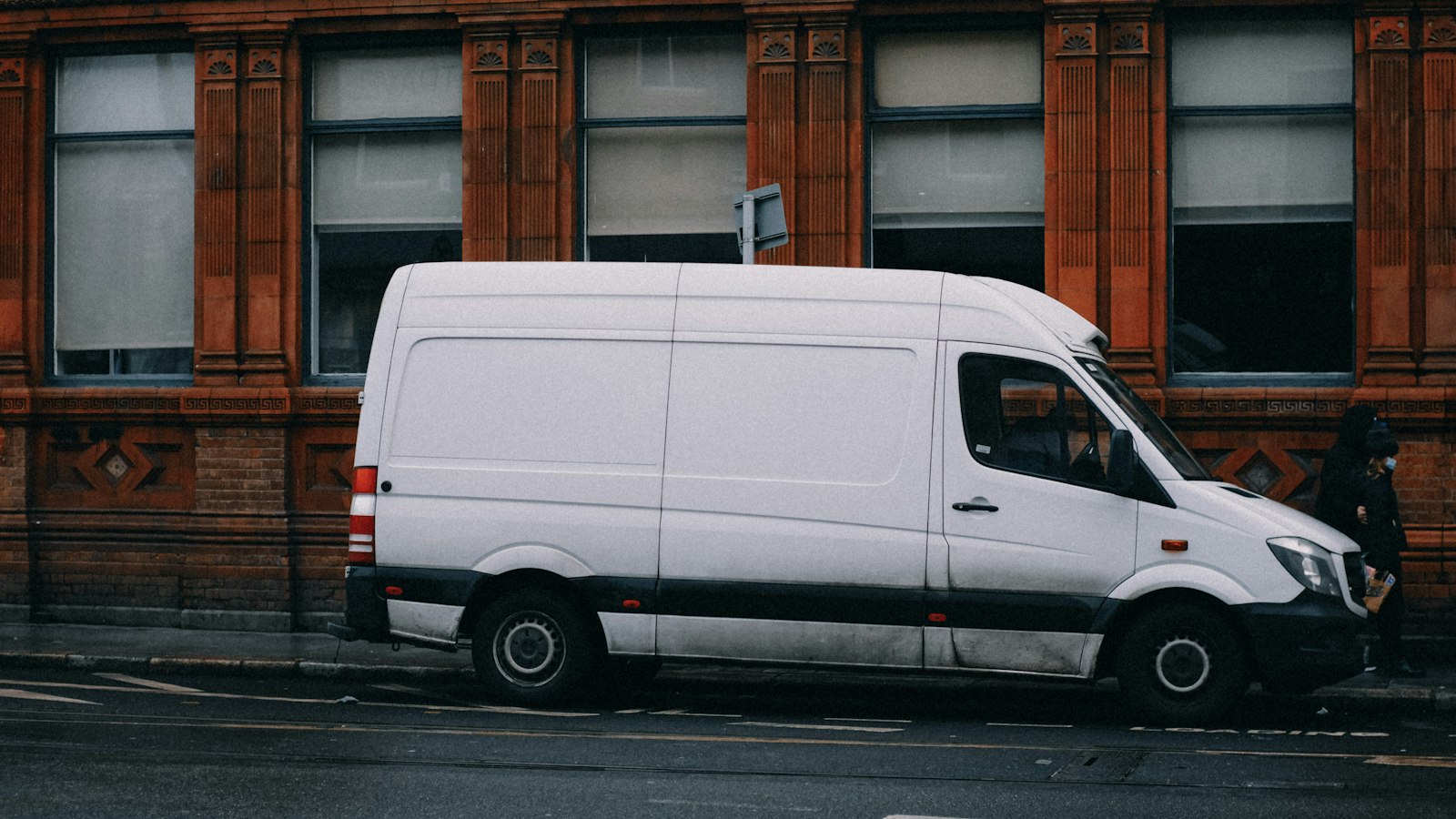 A white panel van parked on a wet street in front of a red-brick building