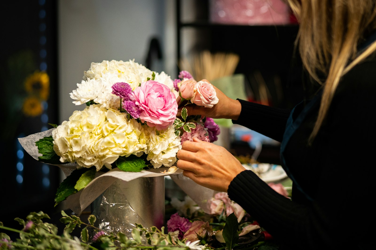 A florist's hands wrapping a hydrangea and rose bouquet in paper