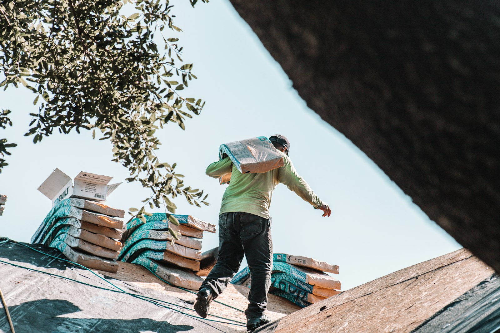 A roofer carrying a bundle of shingles on his shoulder across a roof
