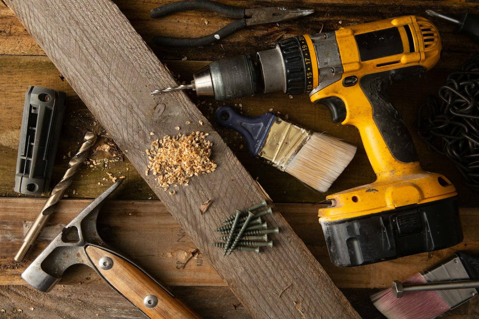 A cordless drill, hammer and screws on a timber workbench