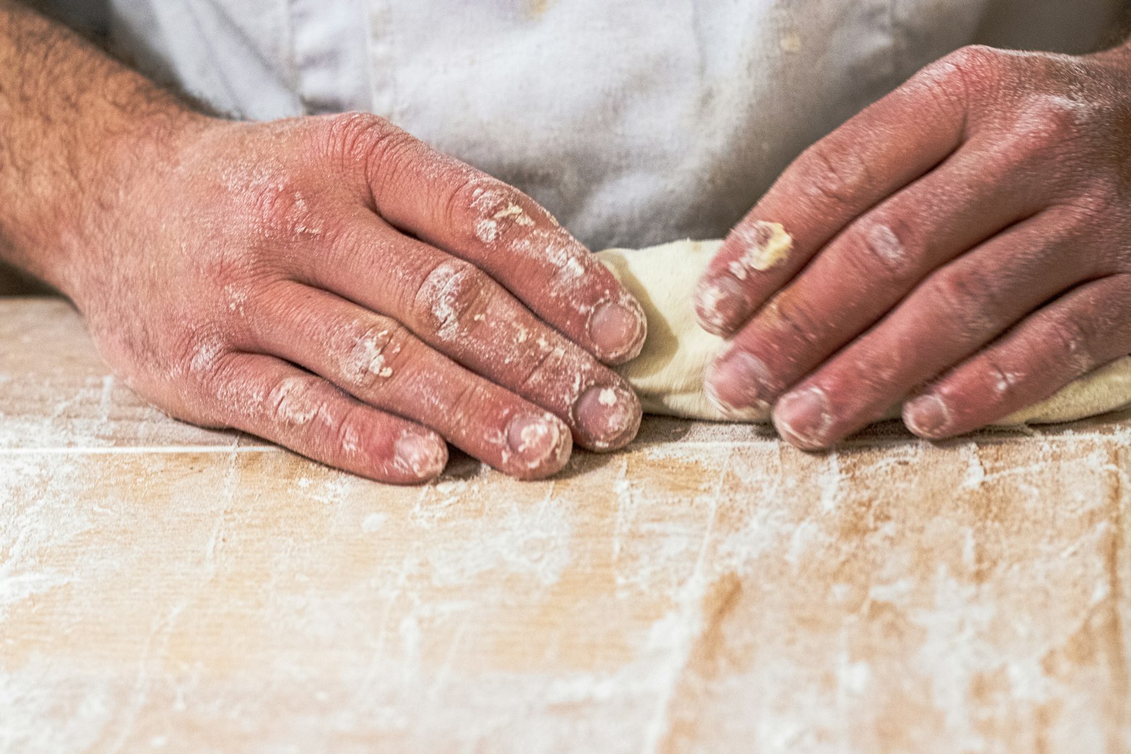 Floury hands pressing dough on a bench