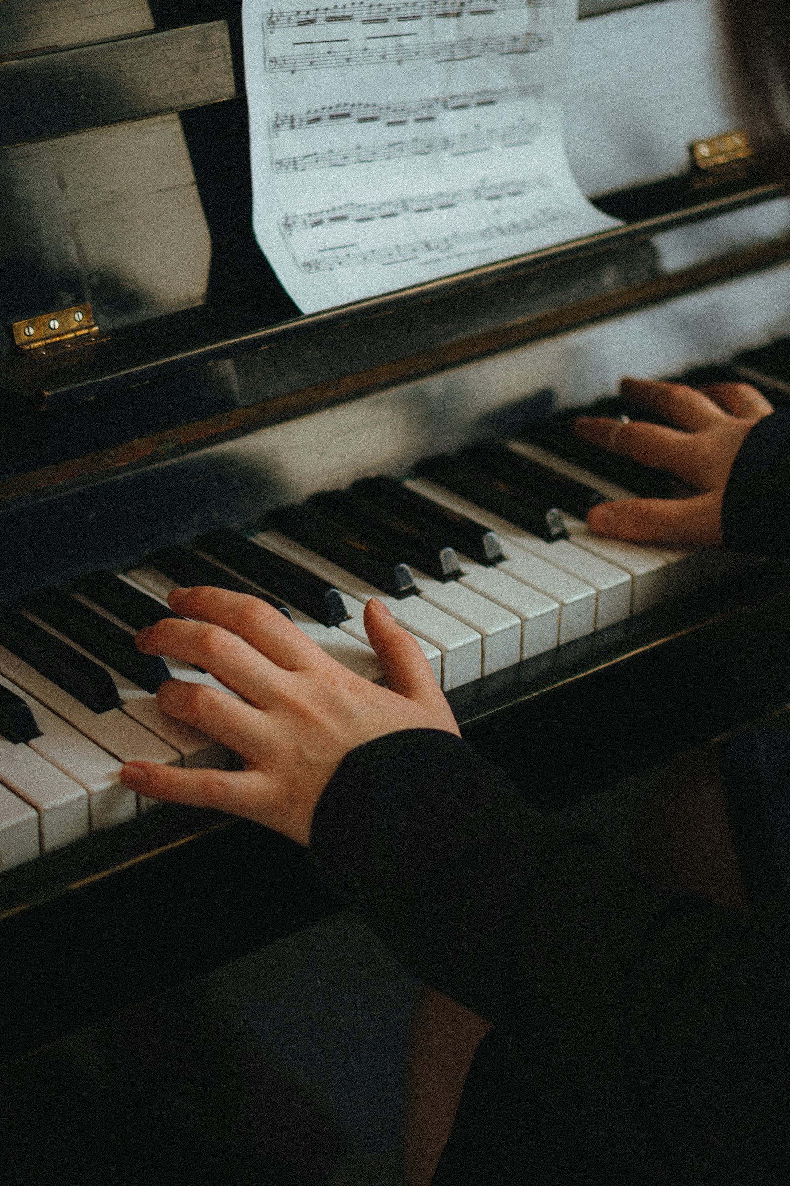 Hands on the keys of an upright piano, sheet music above