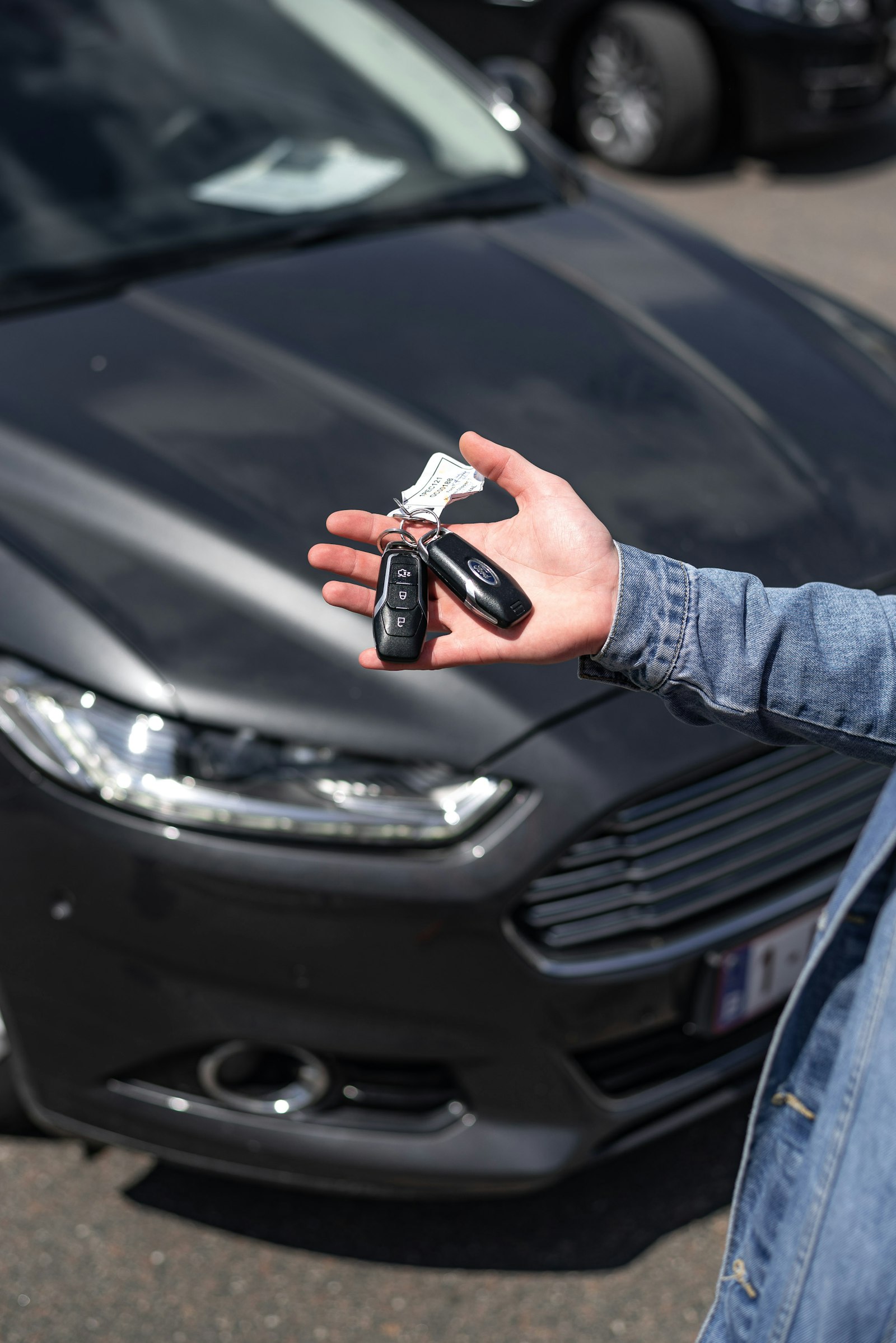 A hand offering keys in front of a dark grey hatchback
