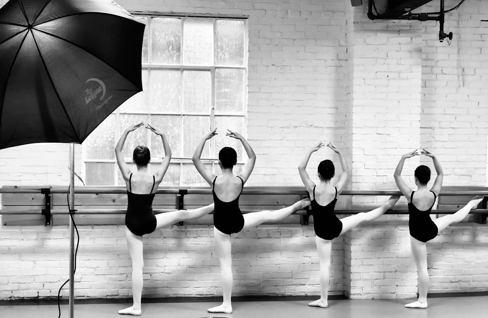 Four ballet students at a wall barre with one leg raised