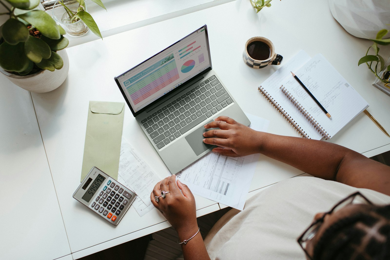 A desk from above with a laptop, receipts and a calculator