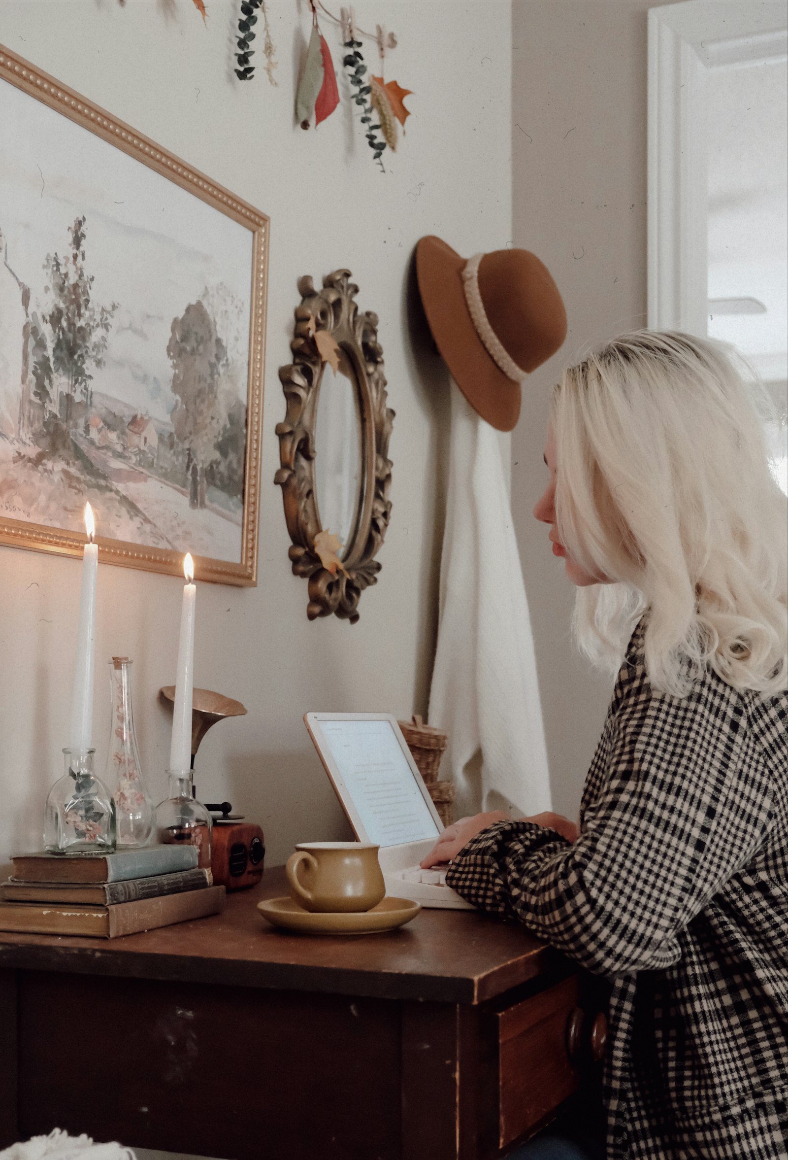 A woman reading at a desk beneath a mirror and two candles