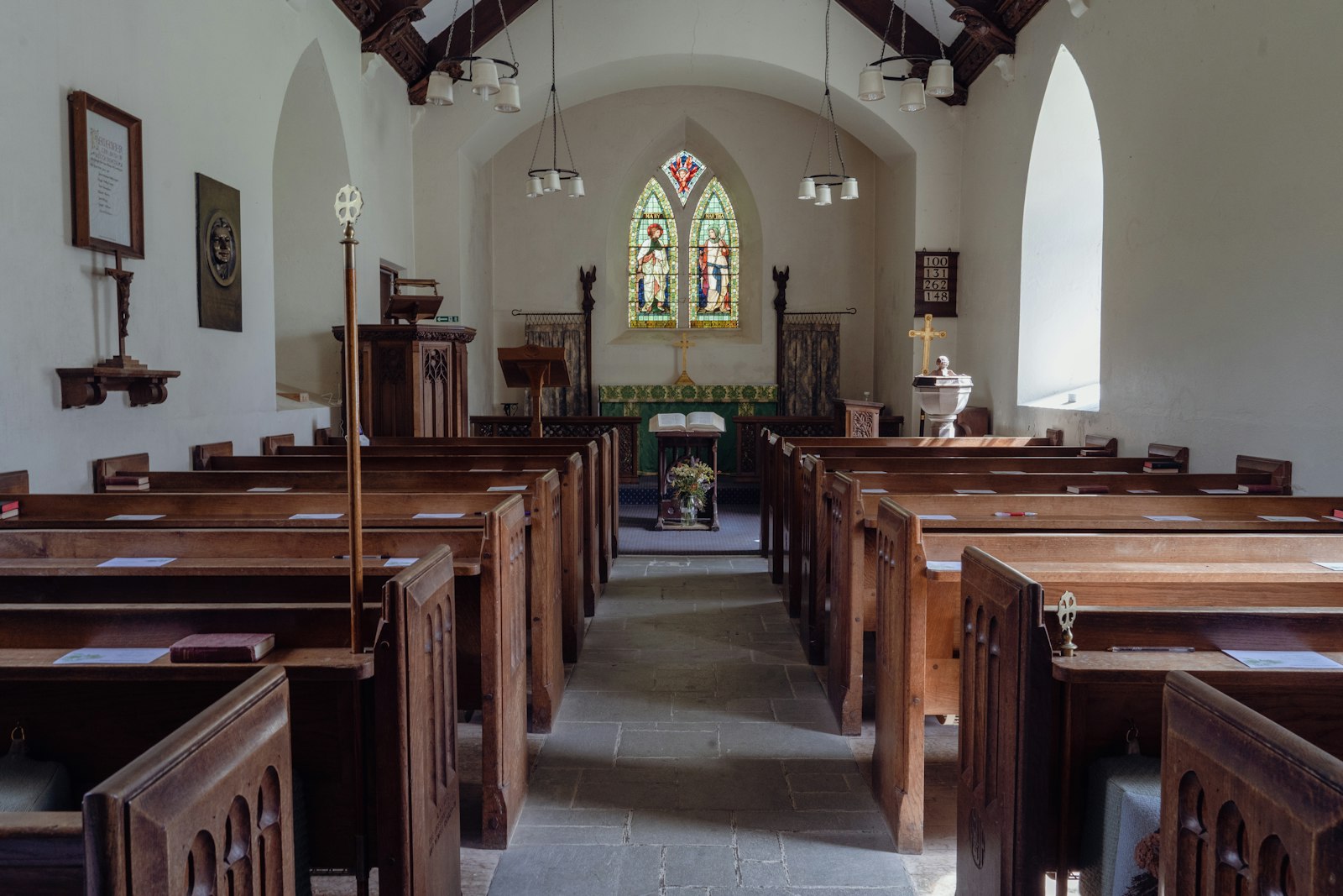 A small whitewashed church interior with wooden pews and a stained-glass window