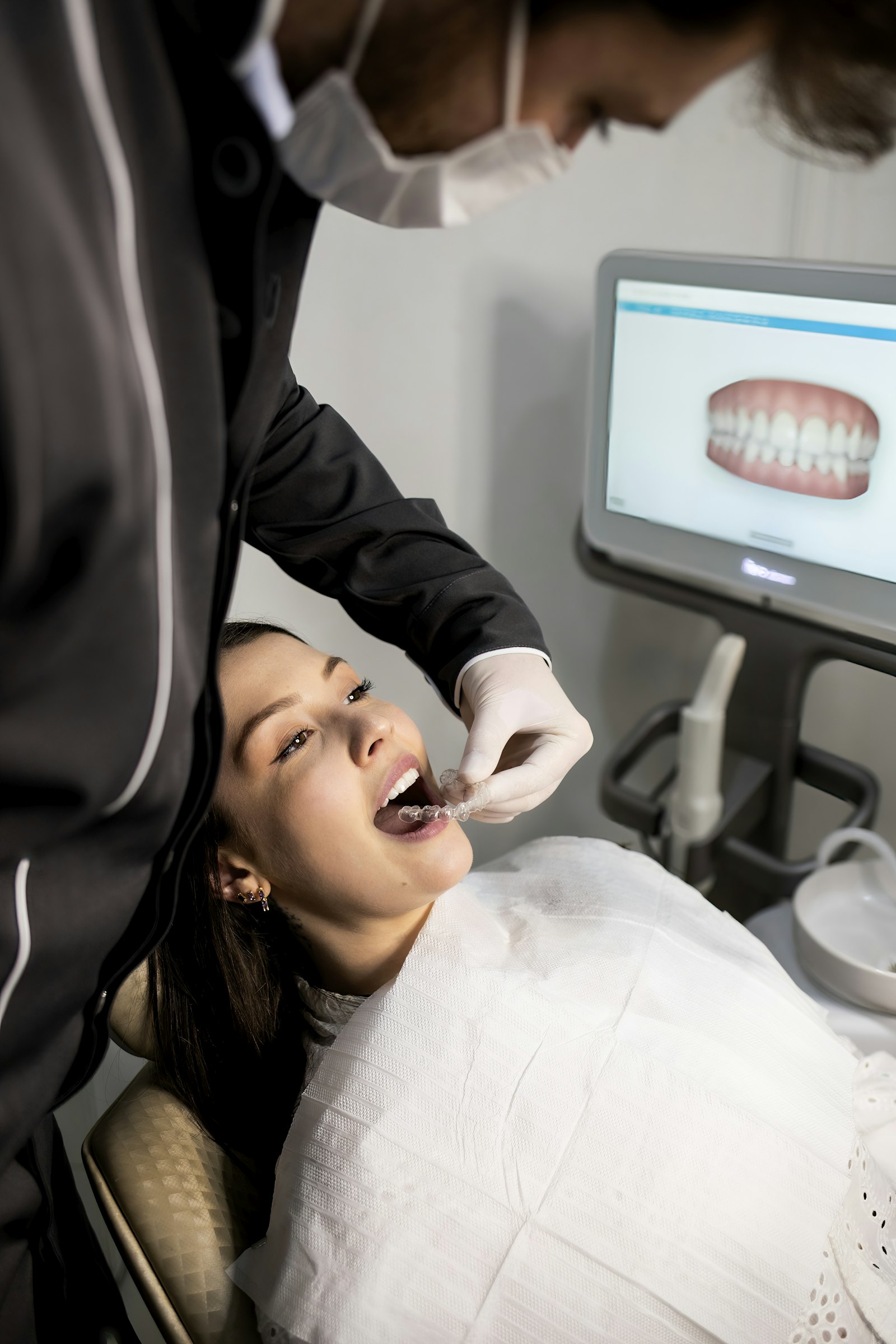 A dentist scanning a patient's teeth with the image on a screen behind