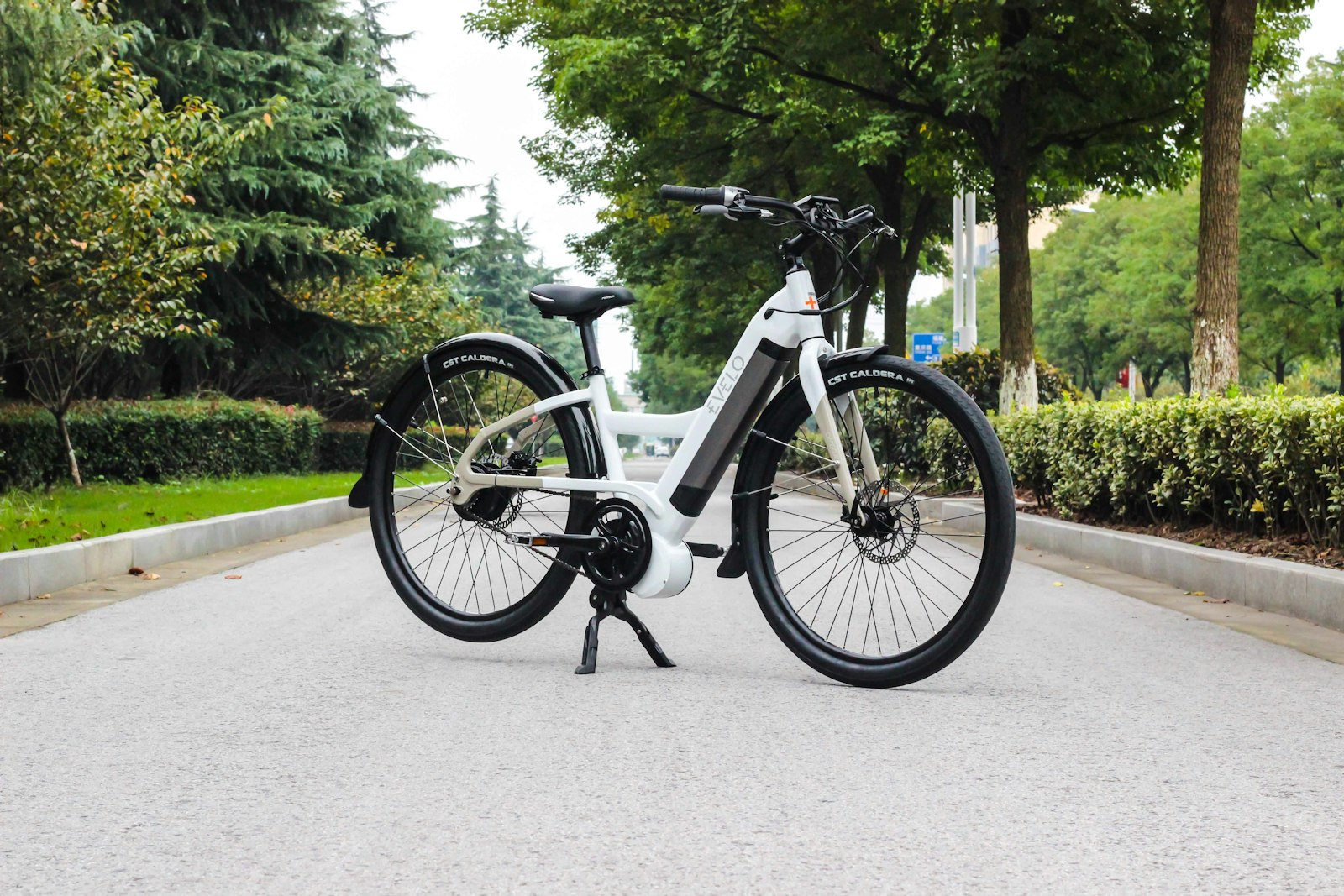 A white step-through e-bike on a tree-lined road