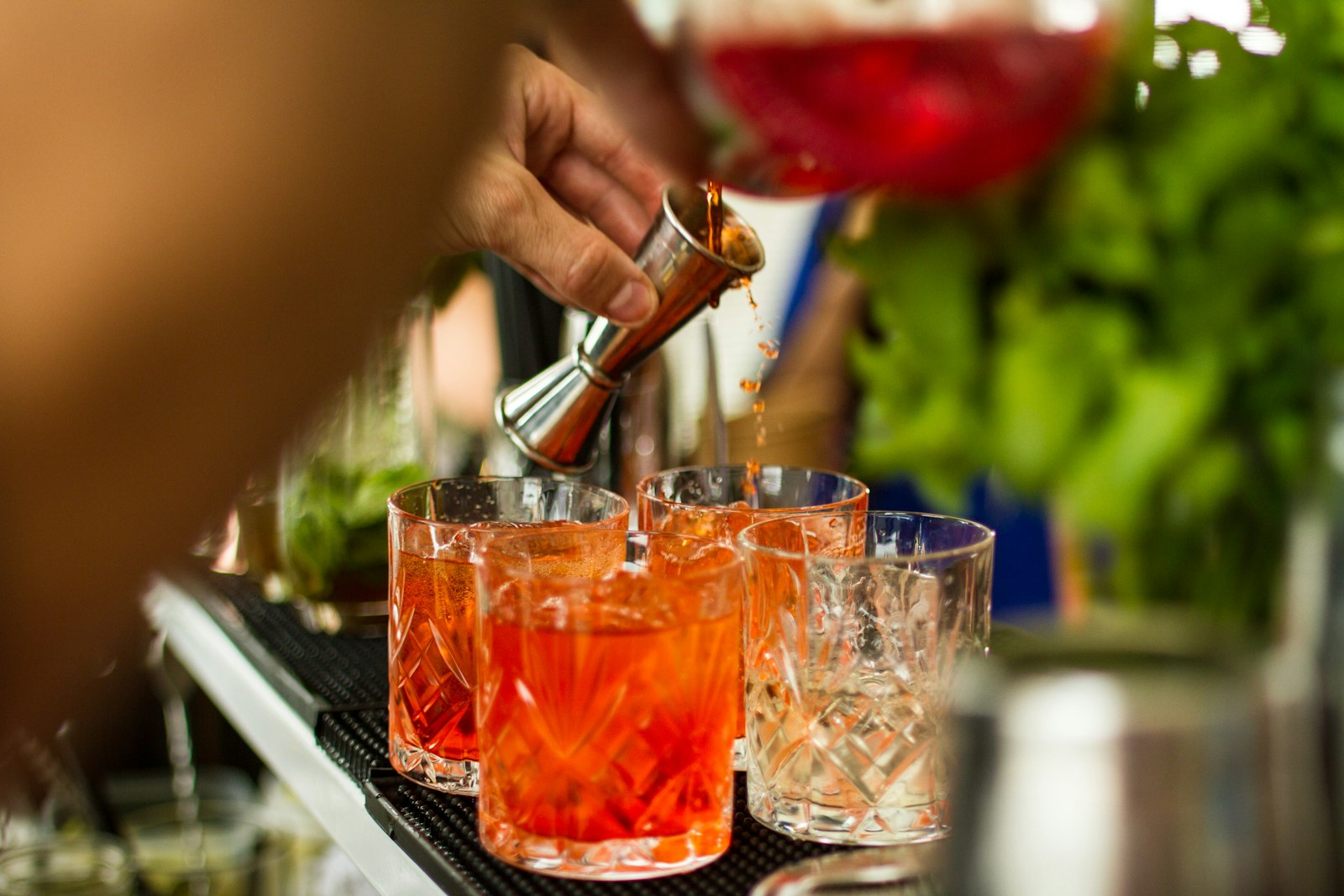 A jigger pouring into a row of red drinks