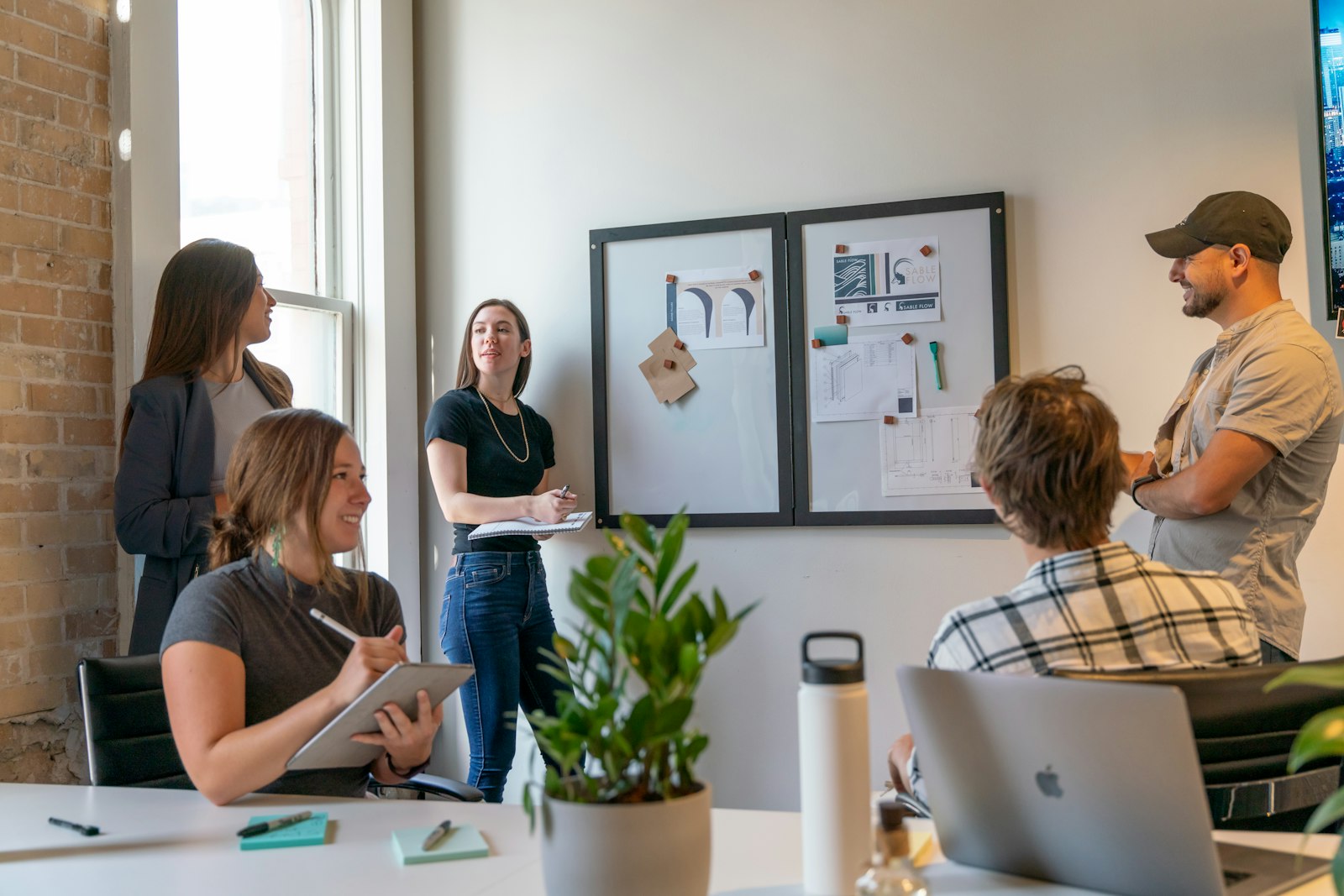 A small team gathered at a pinboard in a sunlit office