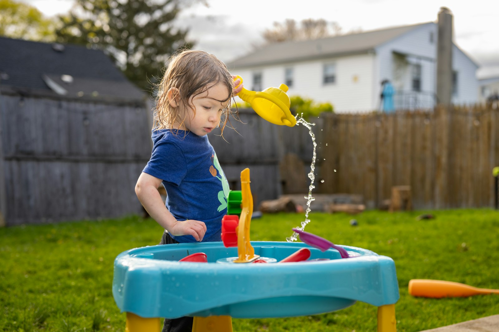 A little girl pouring water at a water-play table in the garden