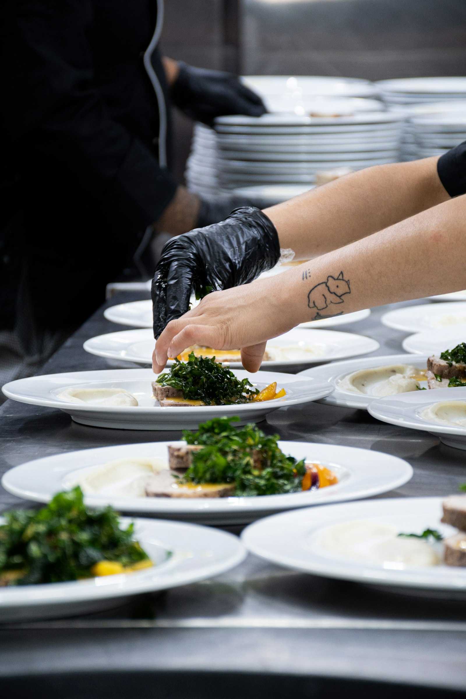 A gloved chef garnishing a long row of plates