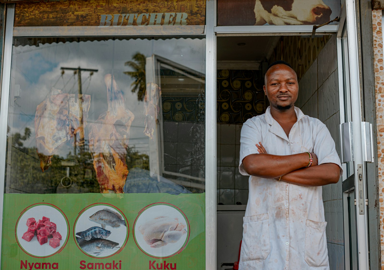 A butcher standing with his arms folded in his shop doorway