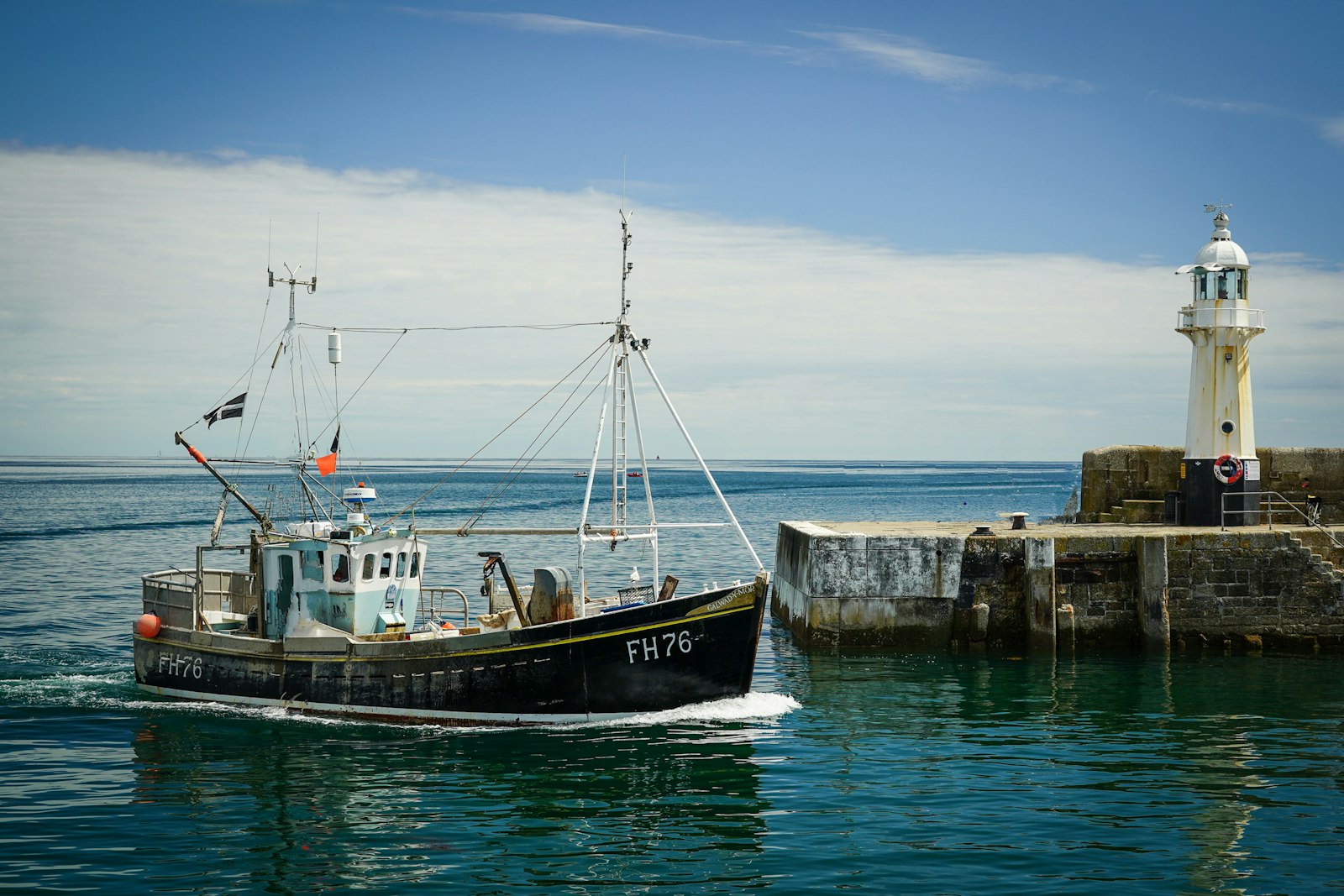 A fishing boat coming into harbour past a lighthouse