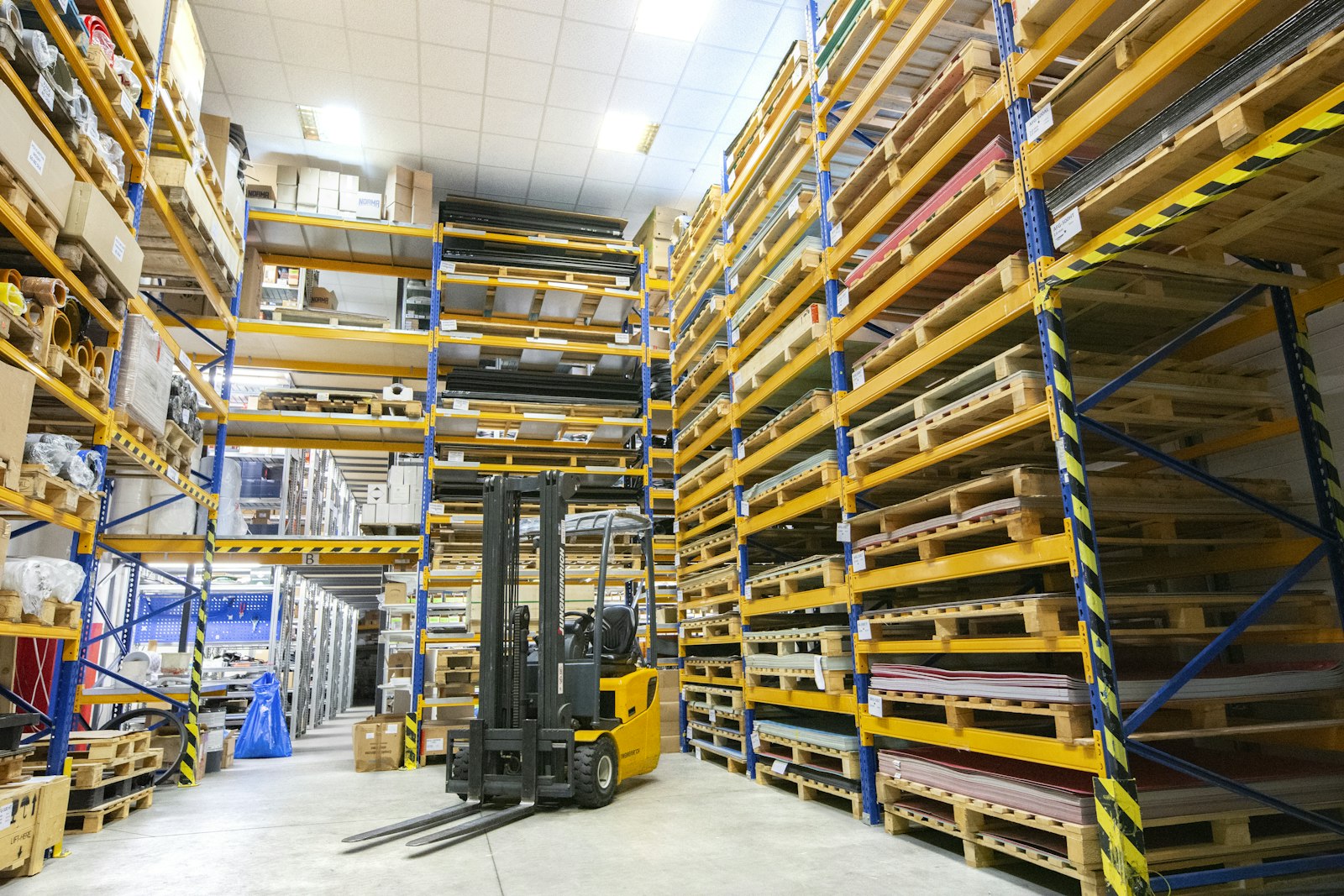 A yellow forklift parked at the end of an aisle of tall pallet racking