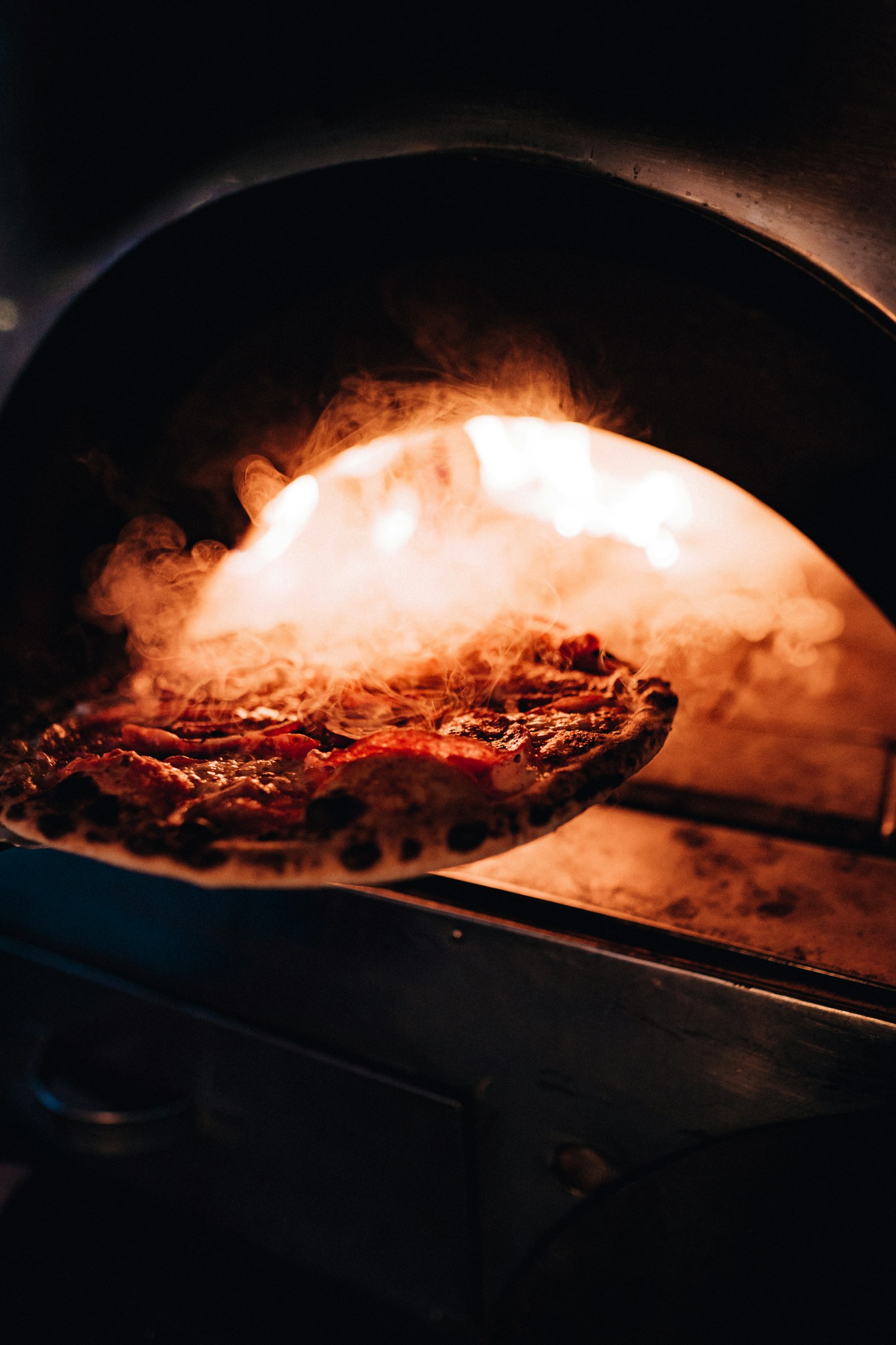 A pizza on a peel coming out of a glowing oven