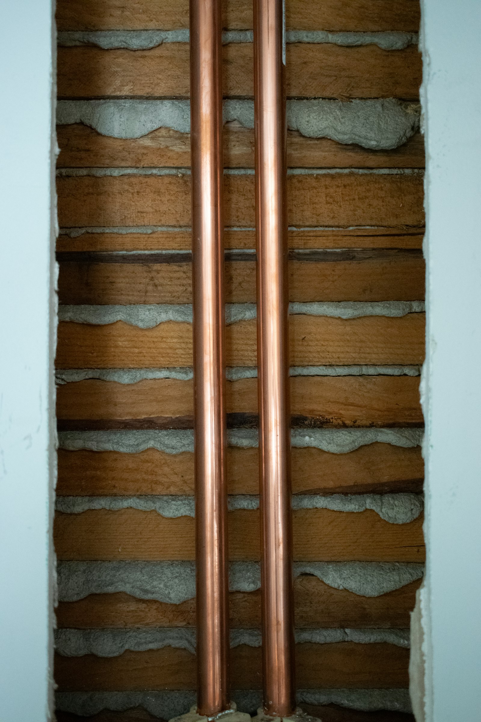 Two copper pipes running vertically through a timber-framed wall