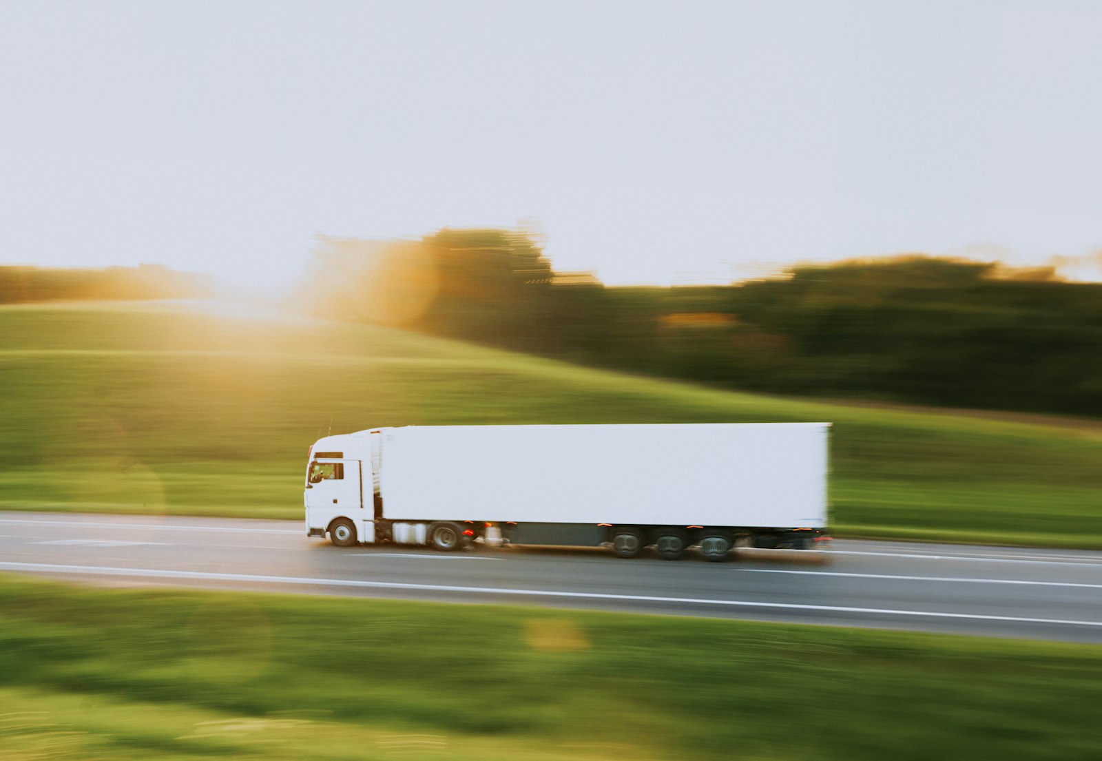 A white articulated lorry on a rural road in low golden-hour sun