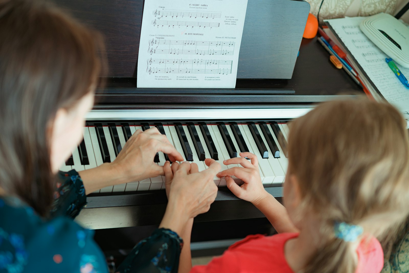 A teacher and a girl at an electric piano, sheet music on the stand