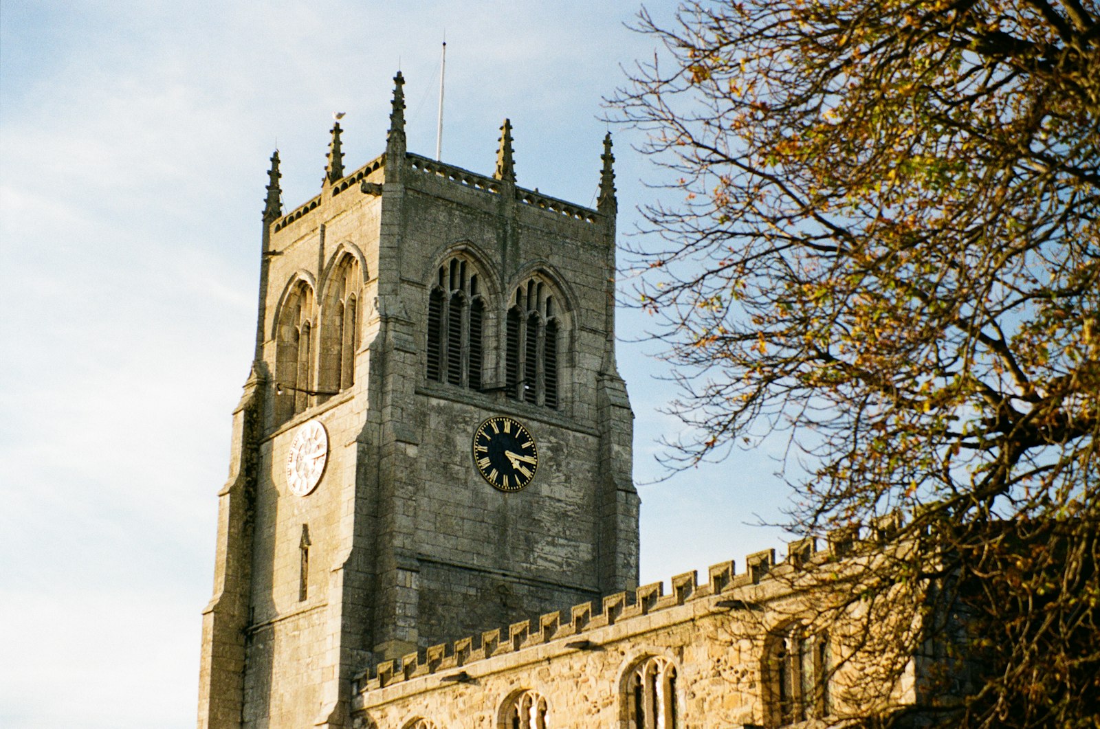 A stone church tower with a clock beside an autumn tree