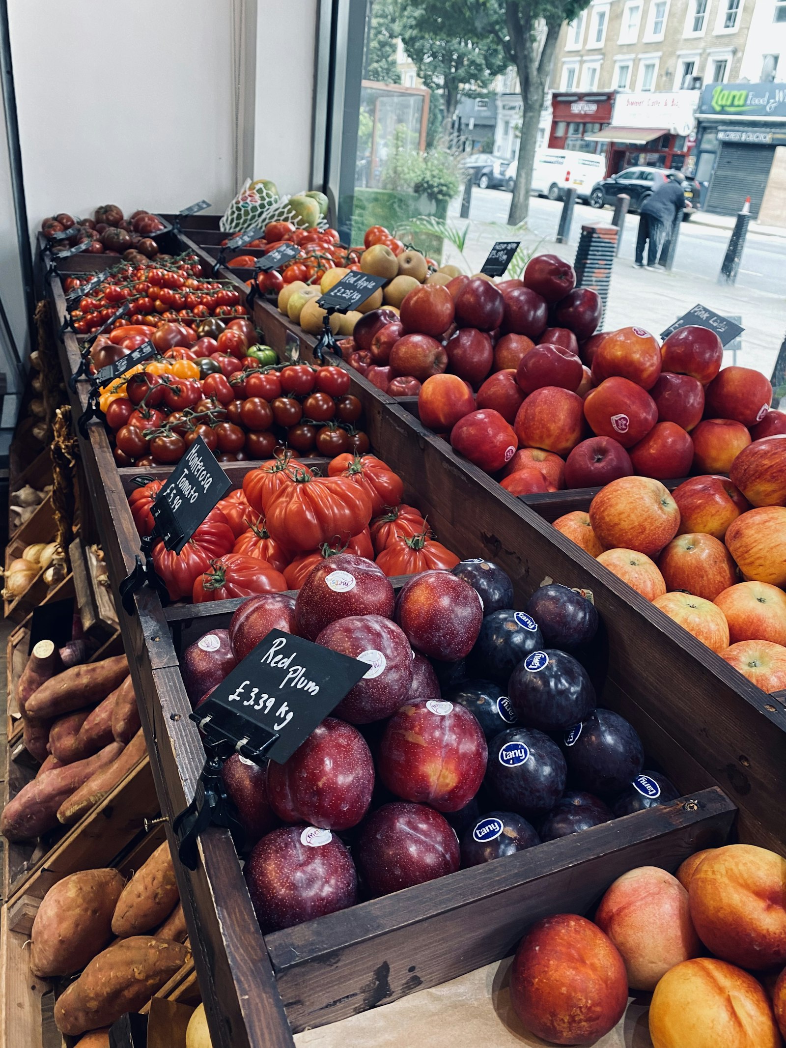 Crates of apples and tomatoes with chalk price cards in a greengrocer's window