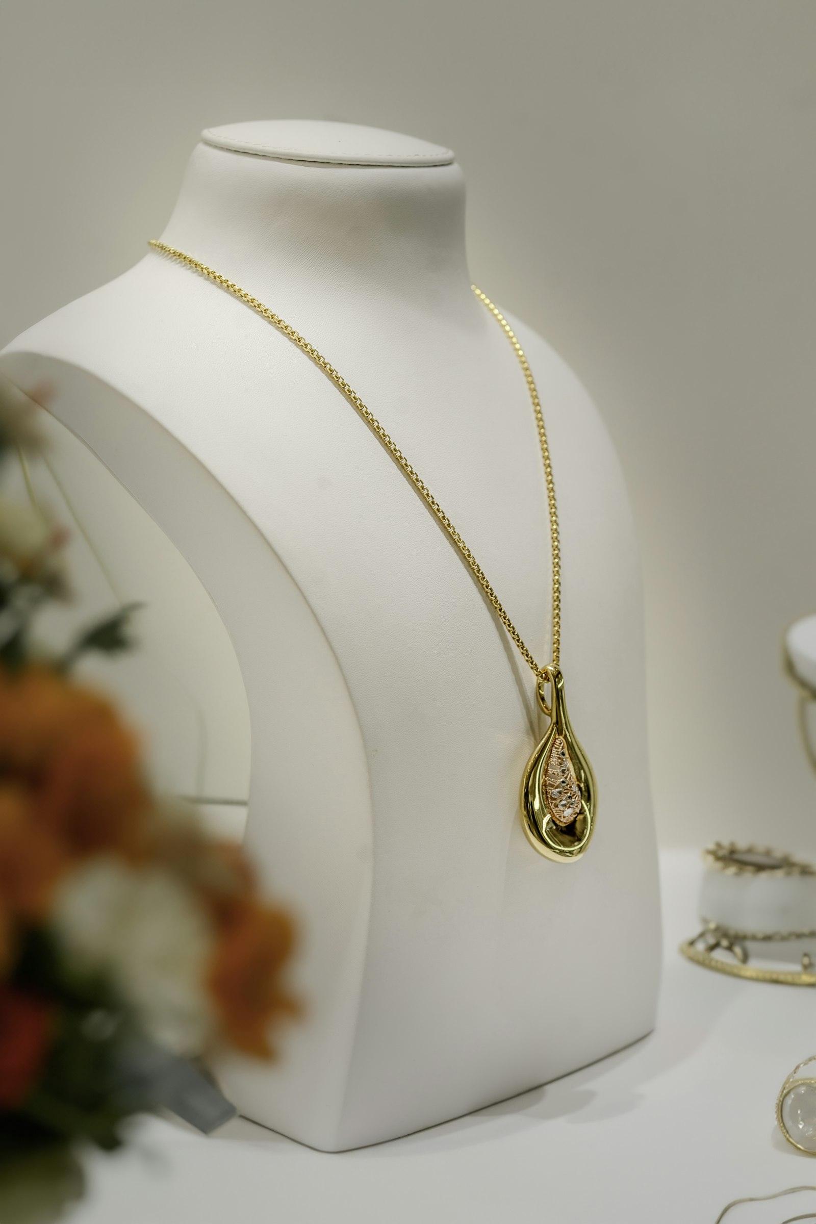 A gold pendant necklace on a white display bust