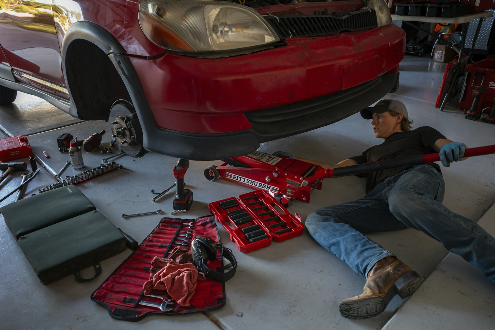 A mechanic lying under a red car with the wheel off and tools laid out on the floor