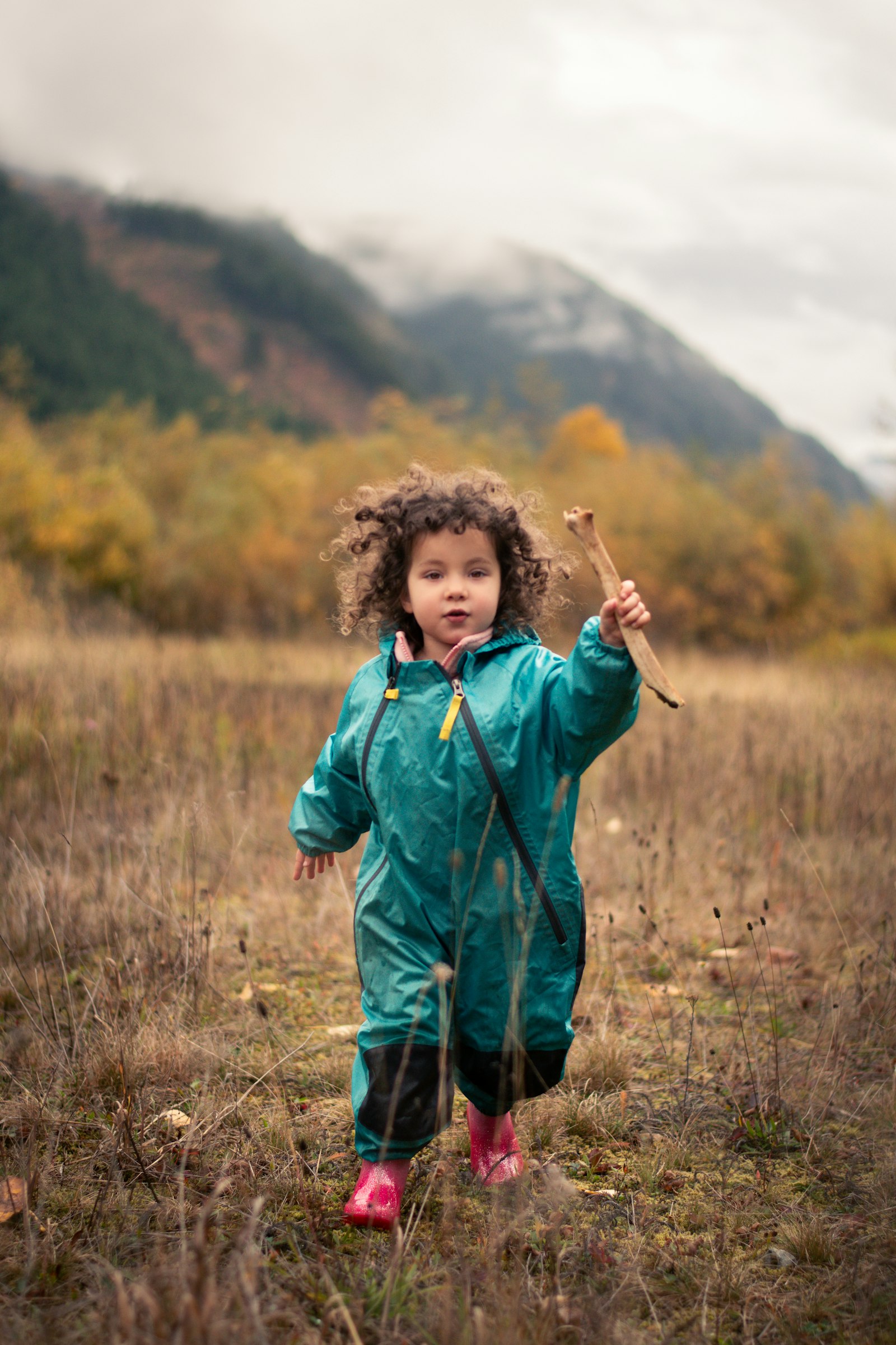 A girl in a green rain suit and pink wellies in a meadow