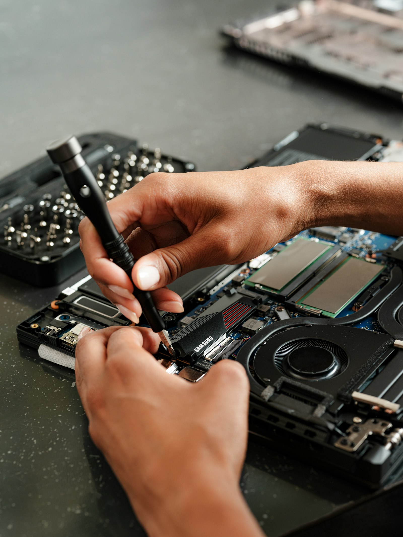 Hands screwing an SSD into an open laptop