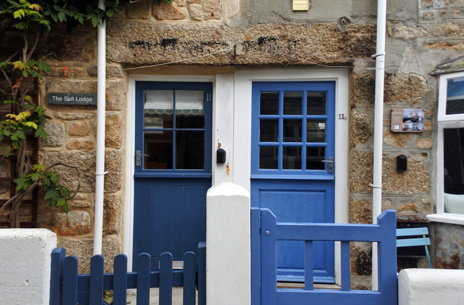 A granite cottage with blue stable doors and a blue gate