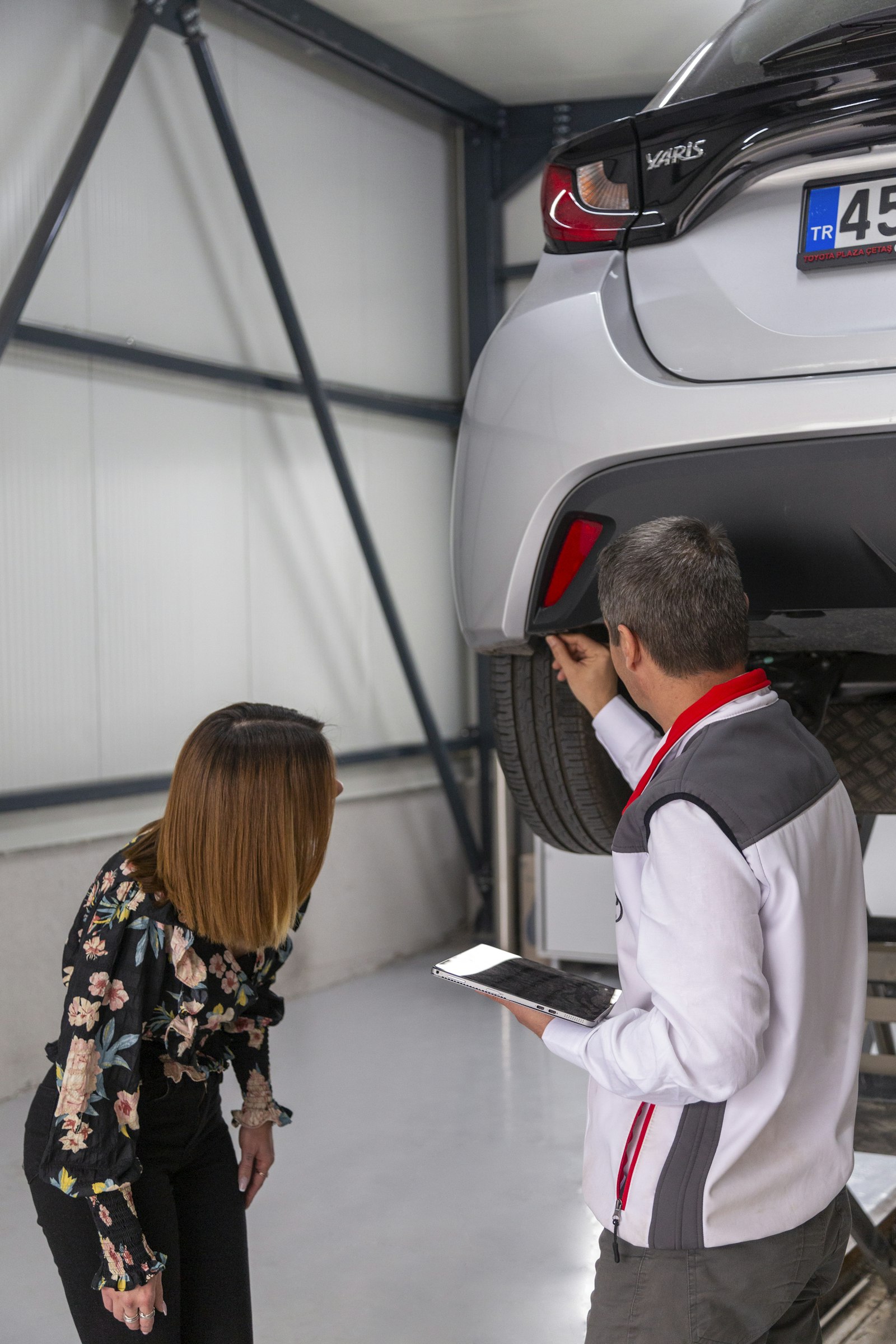 A technician with a tablet showing a customer a car on a lift