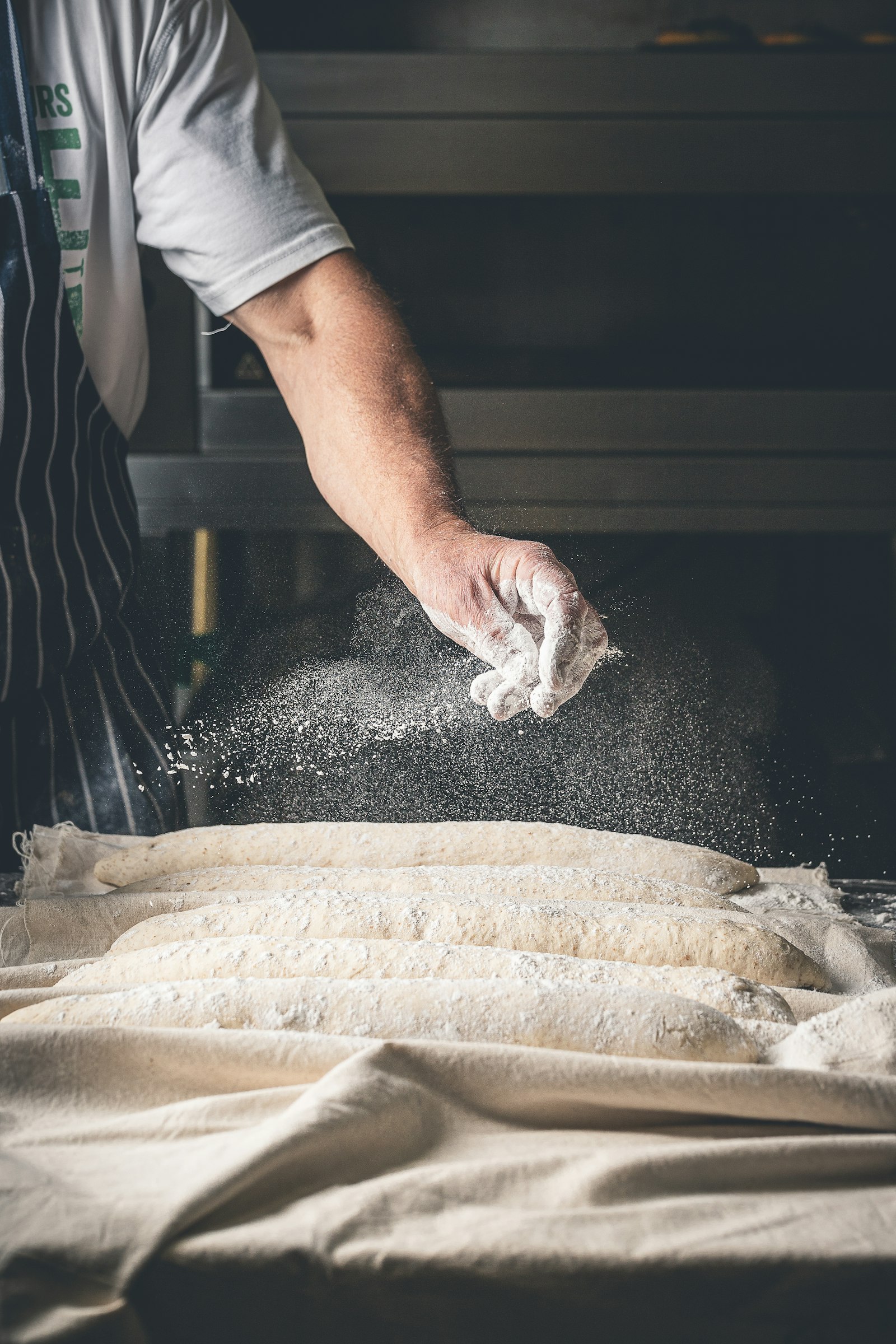 A baker dusting flour over loaves proving in cloth