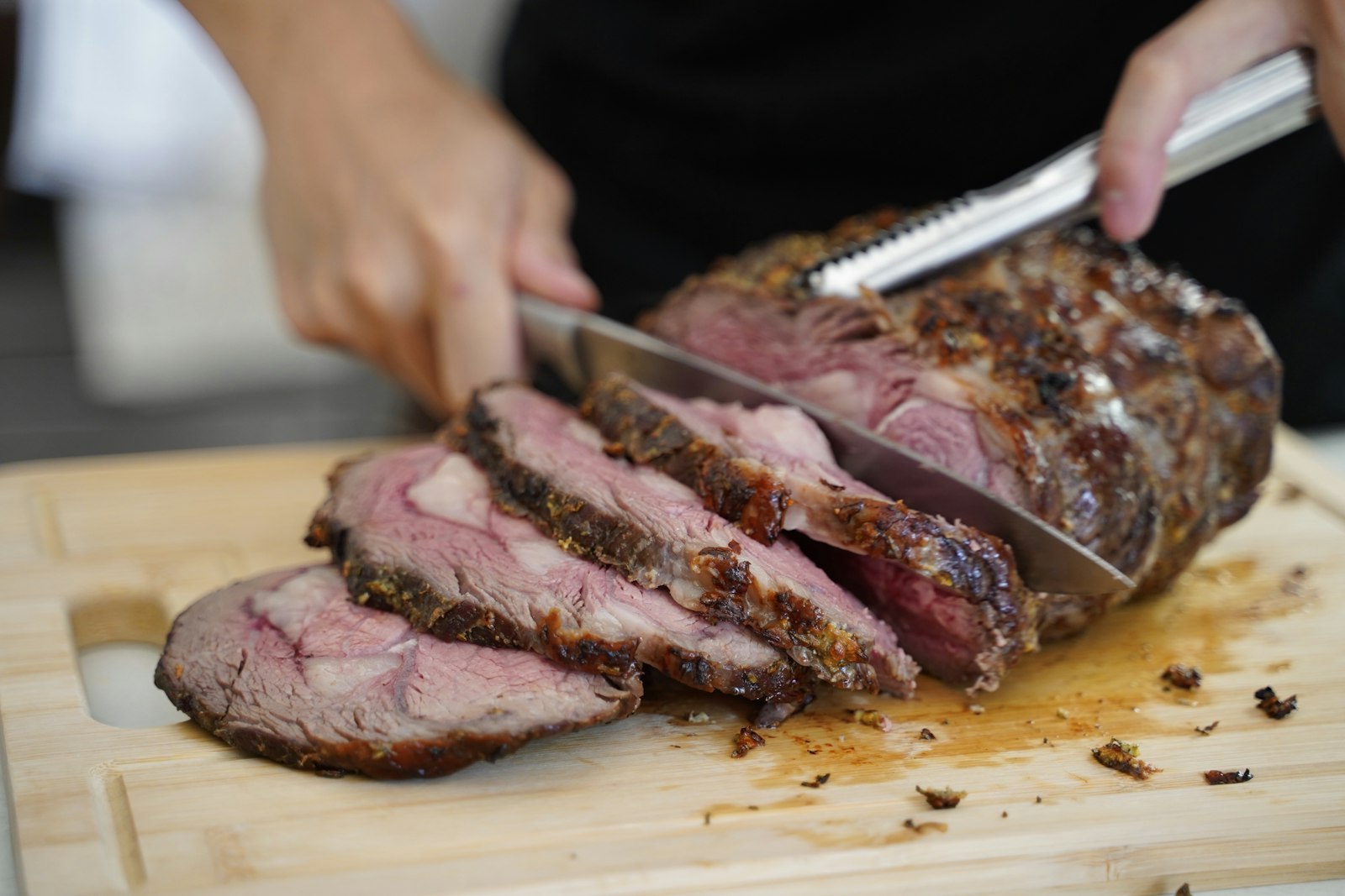 Hands carving a roast beef joint on a board
