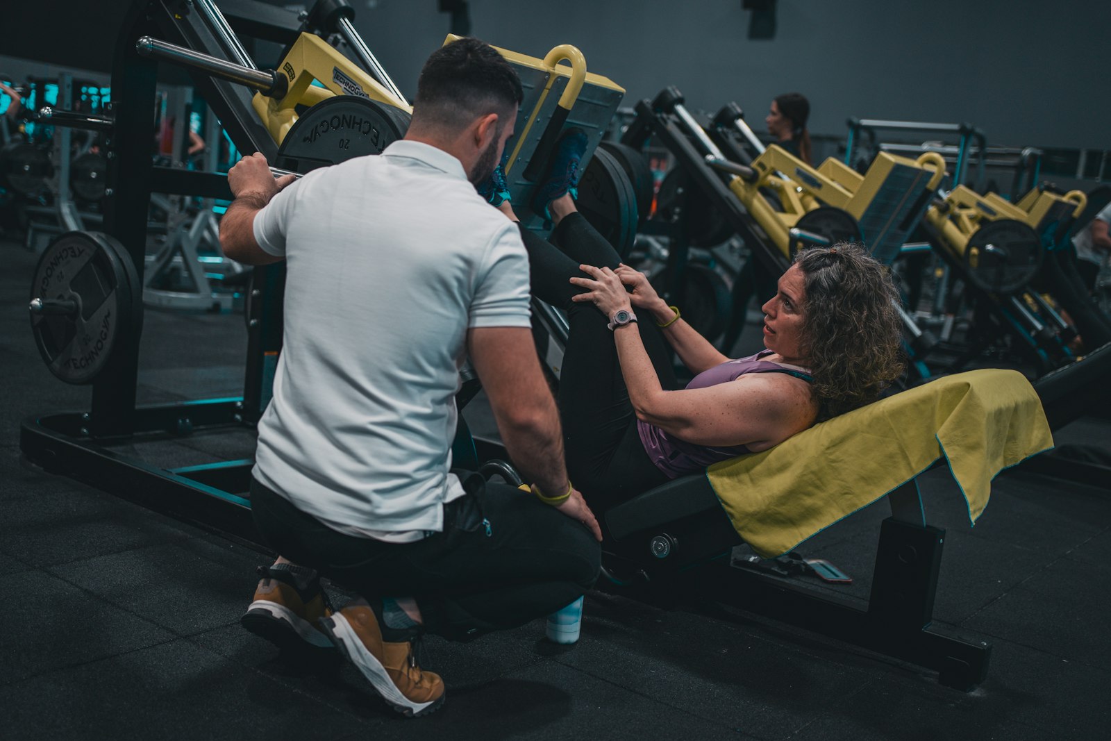 The coach crouched beside a client on a leg press, watching the rep