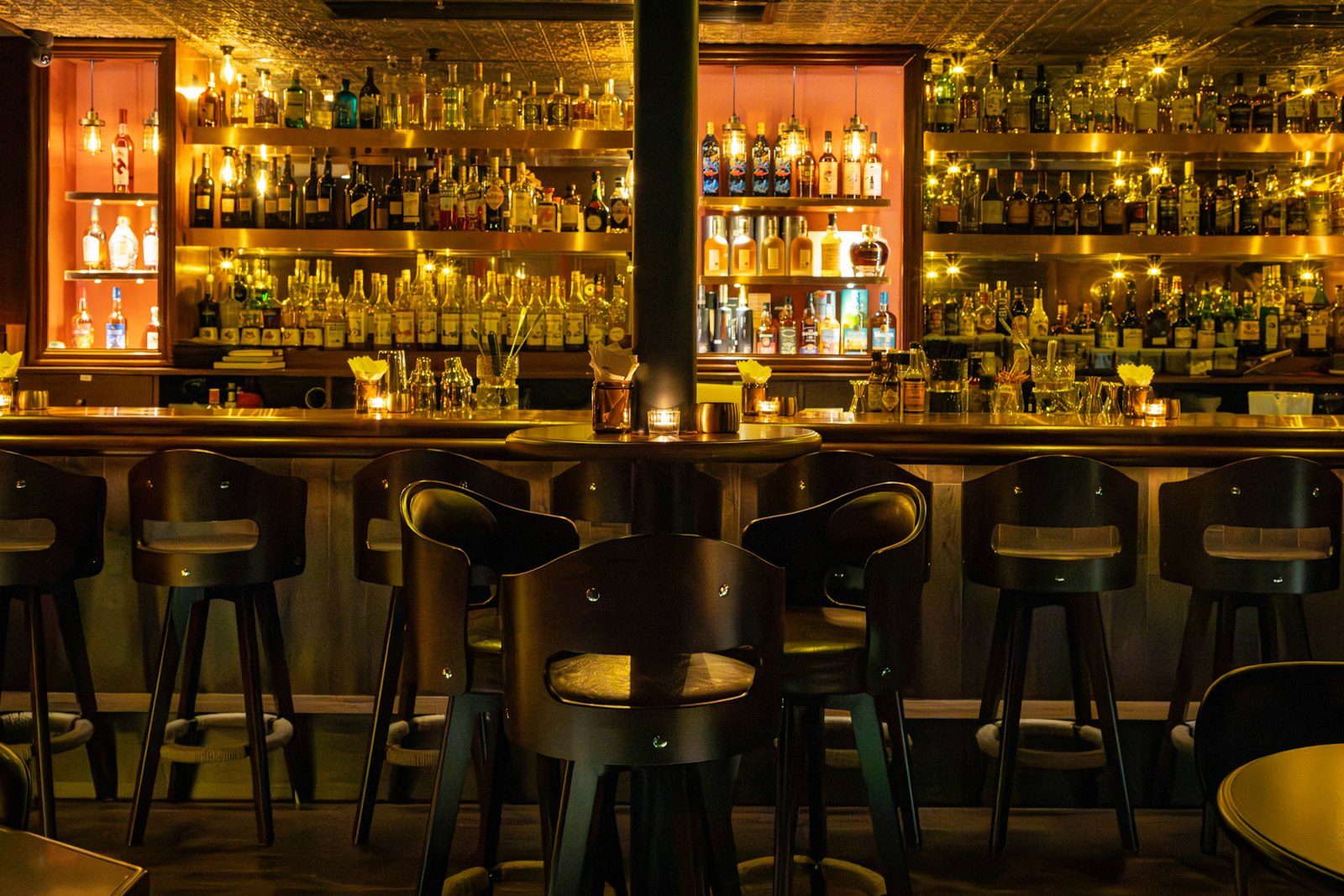 A dim bar with stools and glowing backlit bottles