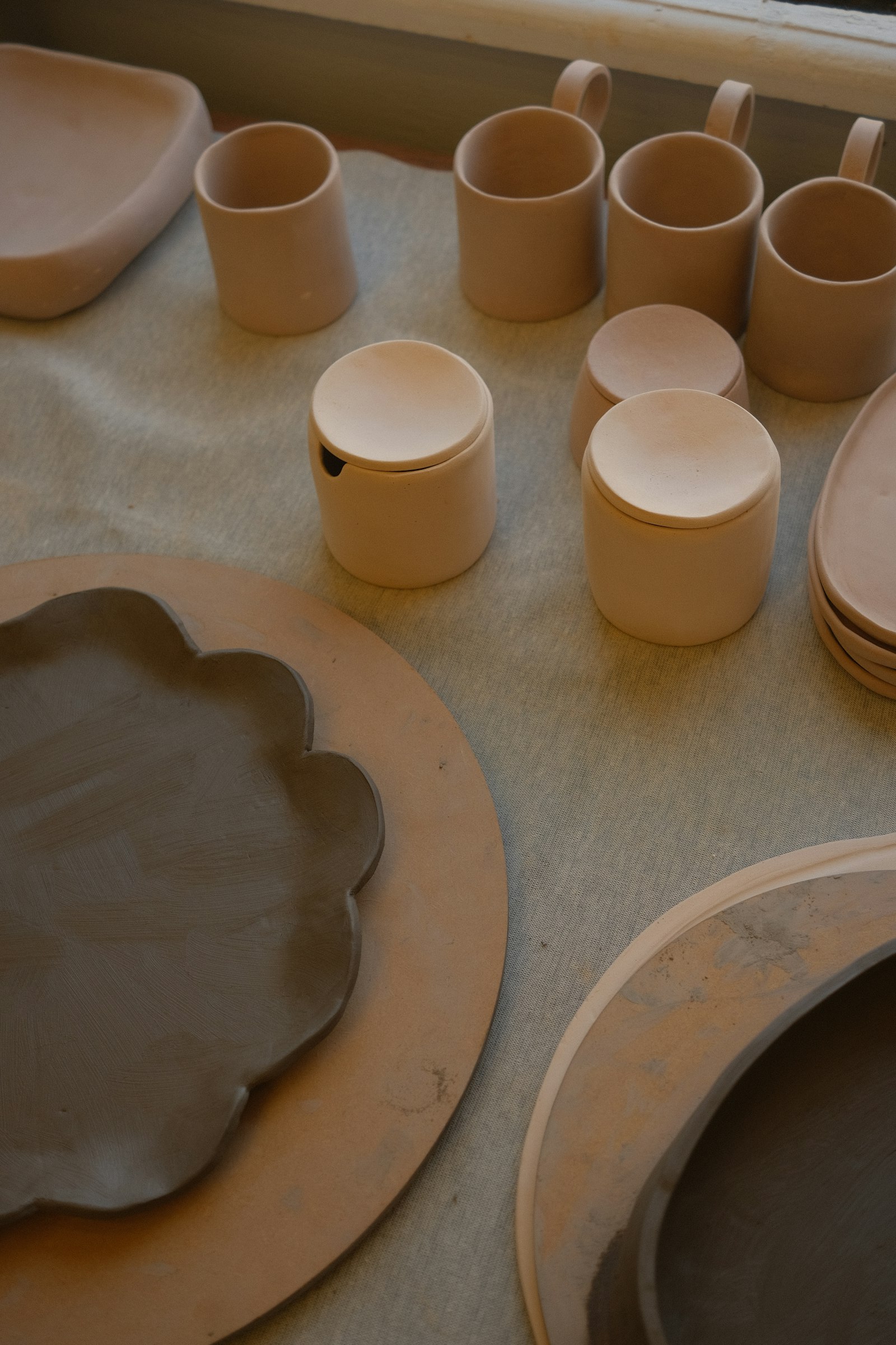 Unglazed mugs and lidded pots on a bench in window light