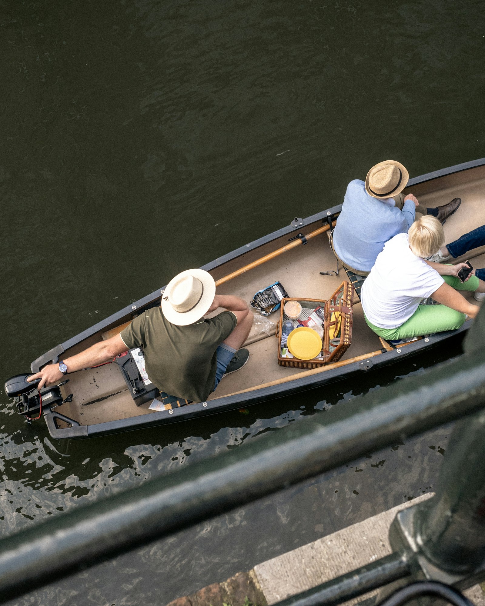 Three people in sun hats in a small boat with a picnic basket