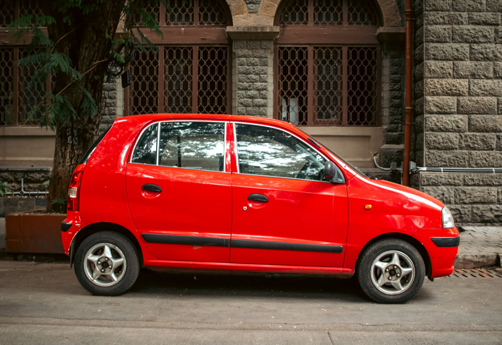 A small red hatchback parked beside an old stone building